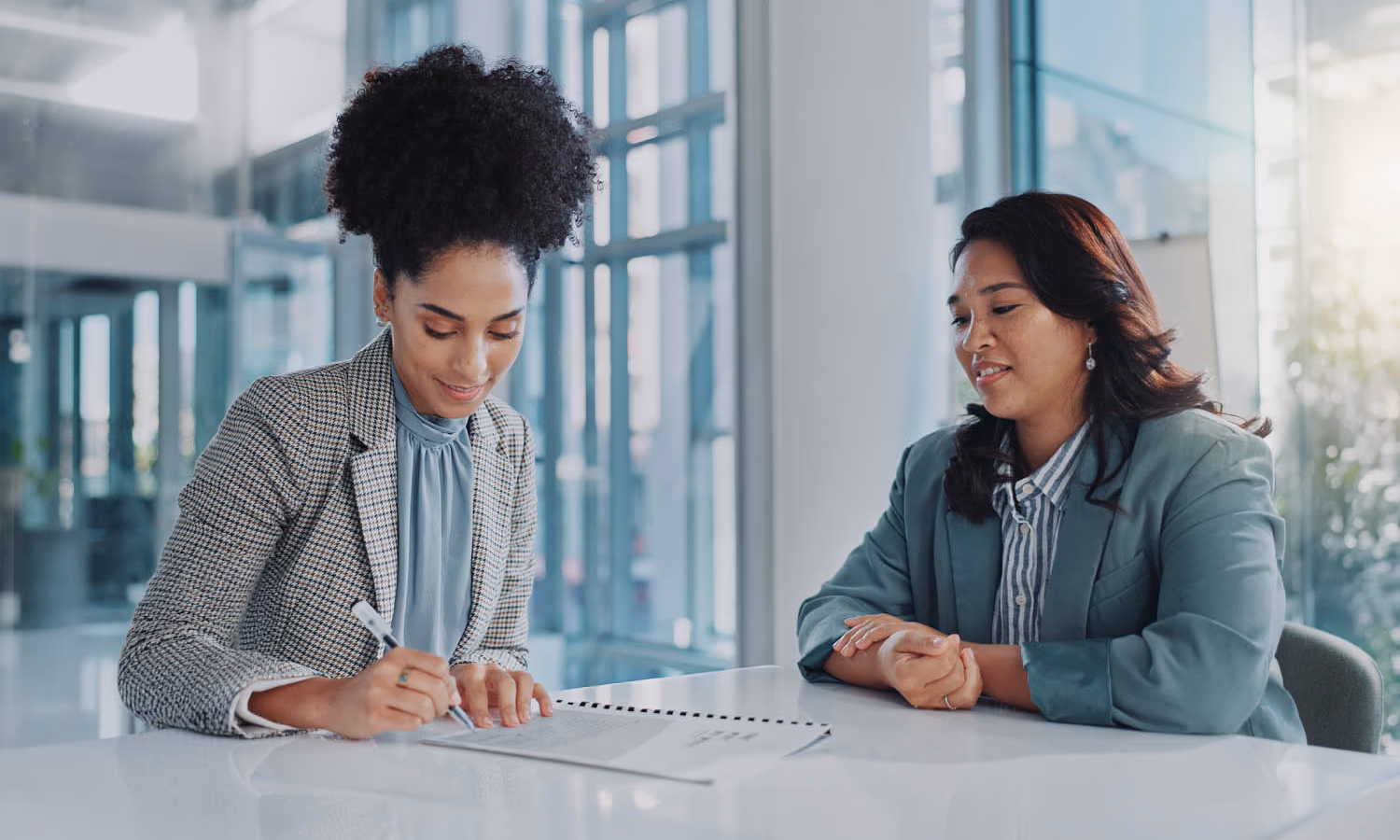 Two businesswomen at a table. One of them is signing a document