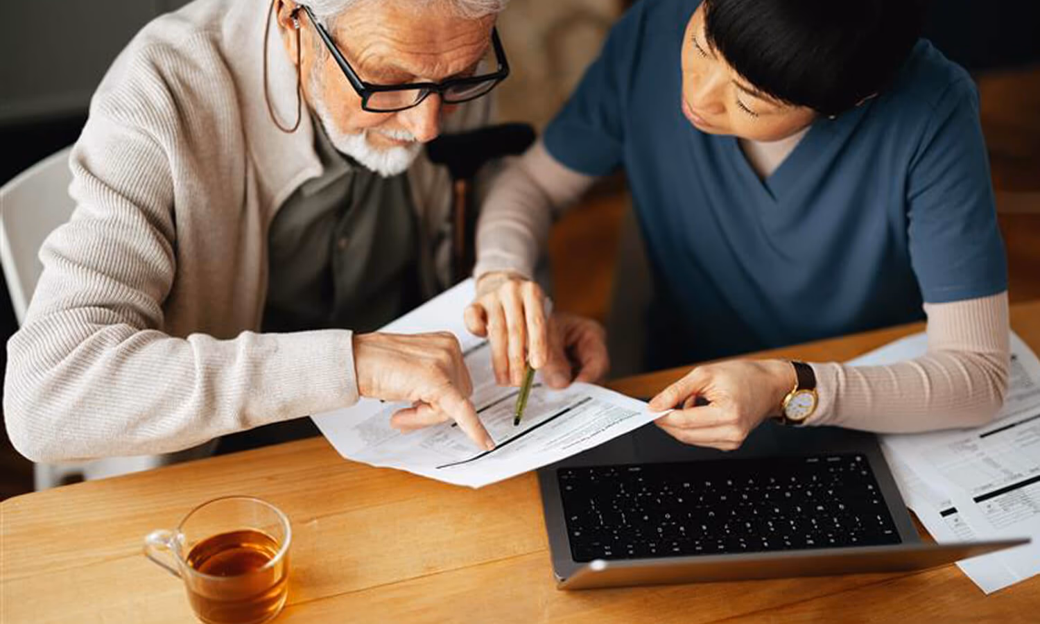 From Above Photo Of A Senior Man Using A Laptop Computer And Paying Bills With Serious Nurse
