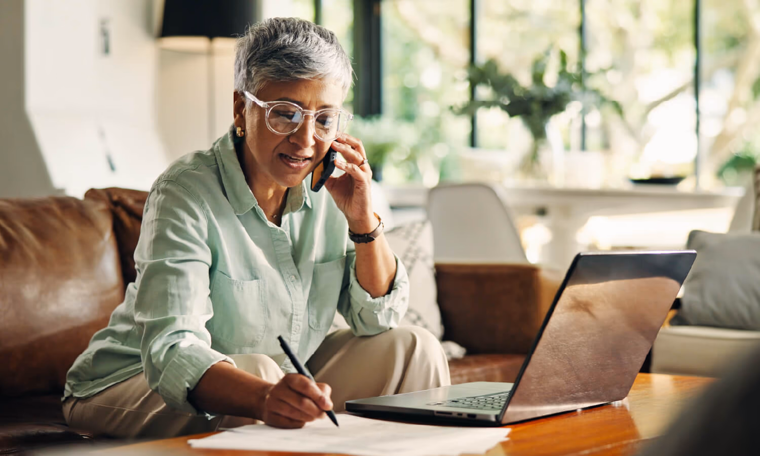 A woman sitting with her laptop and a document, talking on the phone