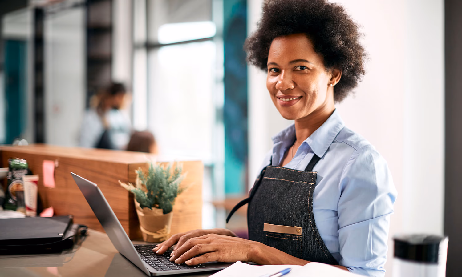 A small business owner wearing an apron smiles as they use a laptop.