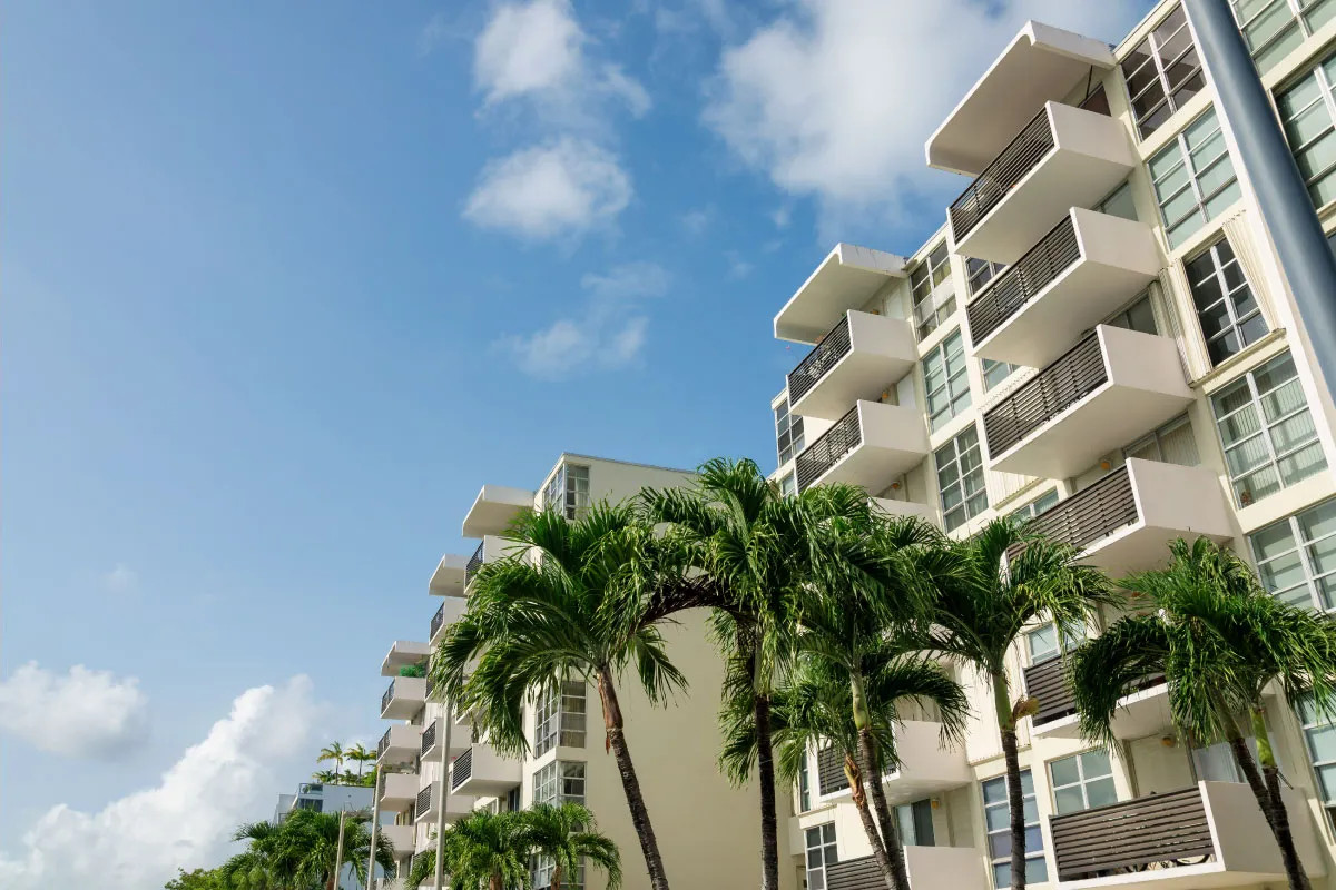 A high-end apartment building with palm trees. The sky is clear and blue.