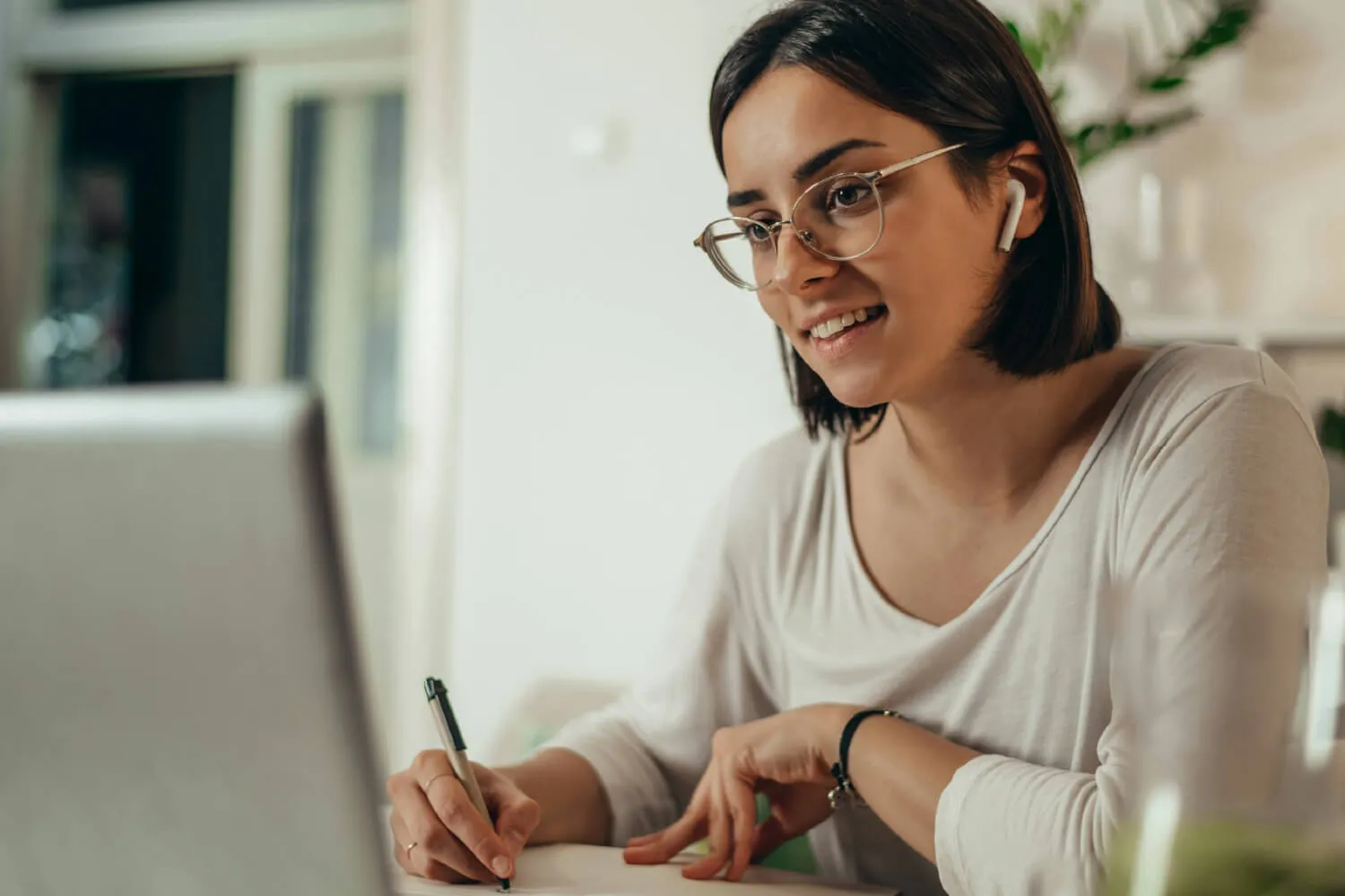 A woman on a video call, taking notes.