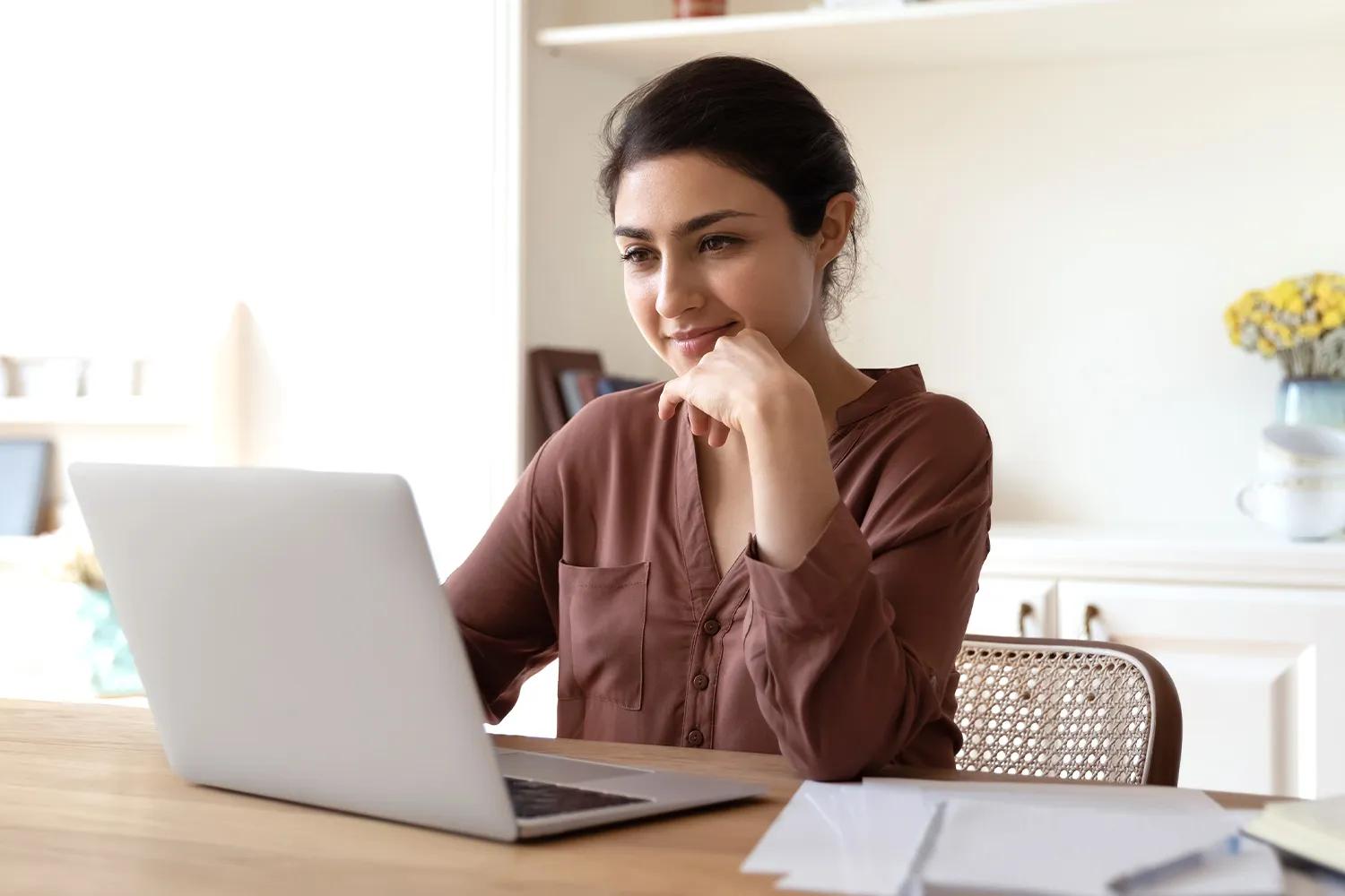 A woman working on a laptop in a bright kitchen