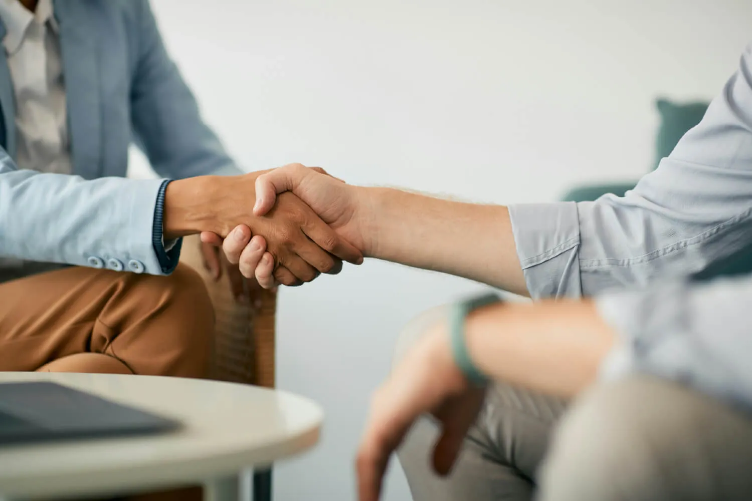 Two people sitting near a table with a laptop on it shake hands