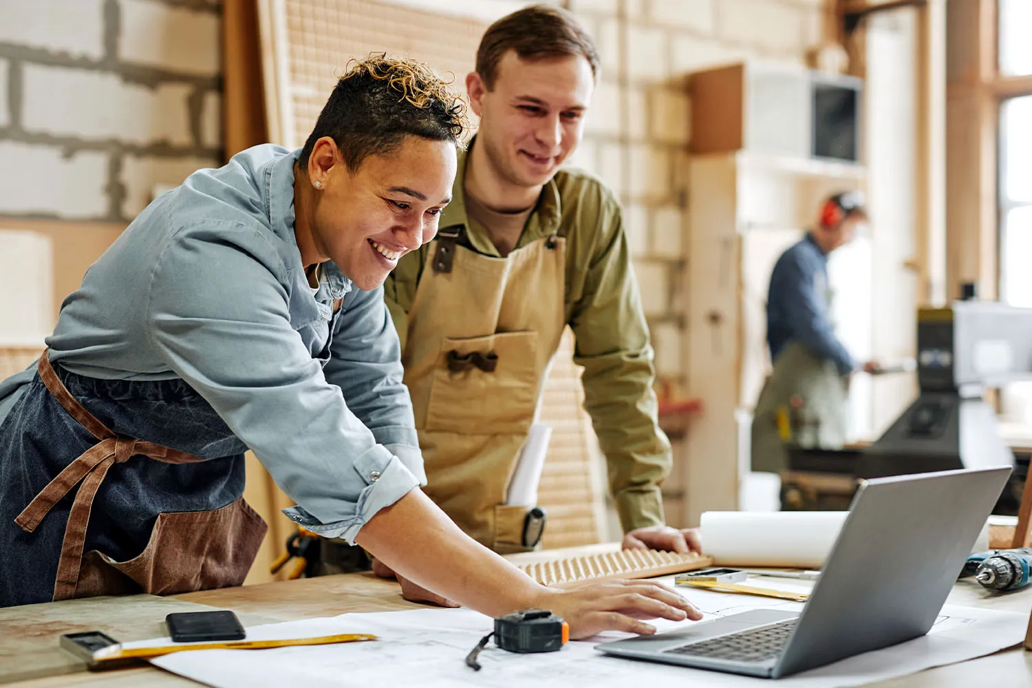 Two craftspeople look at a laptop in a carpentry shop