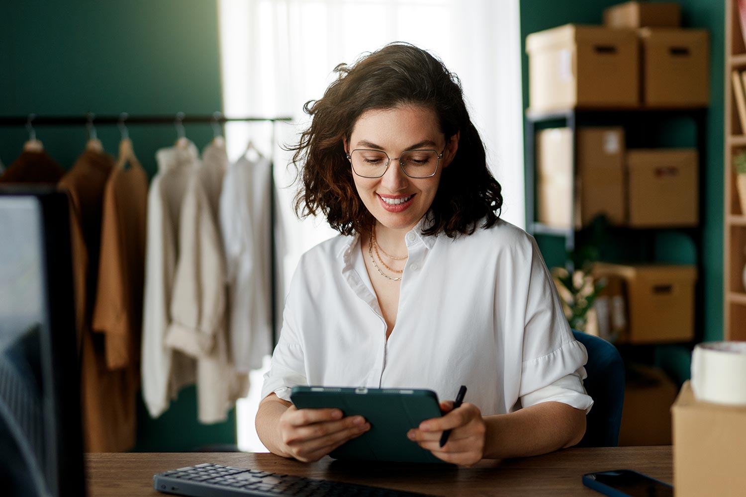 A woman sitting in her office in front of a computer, holding a tablet.