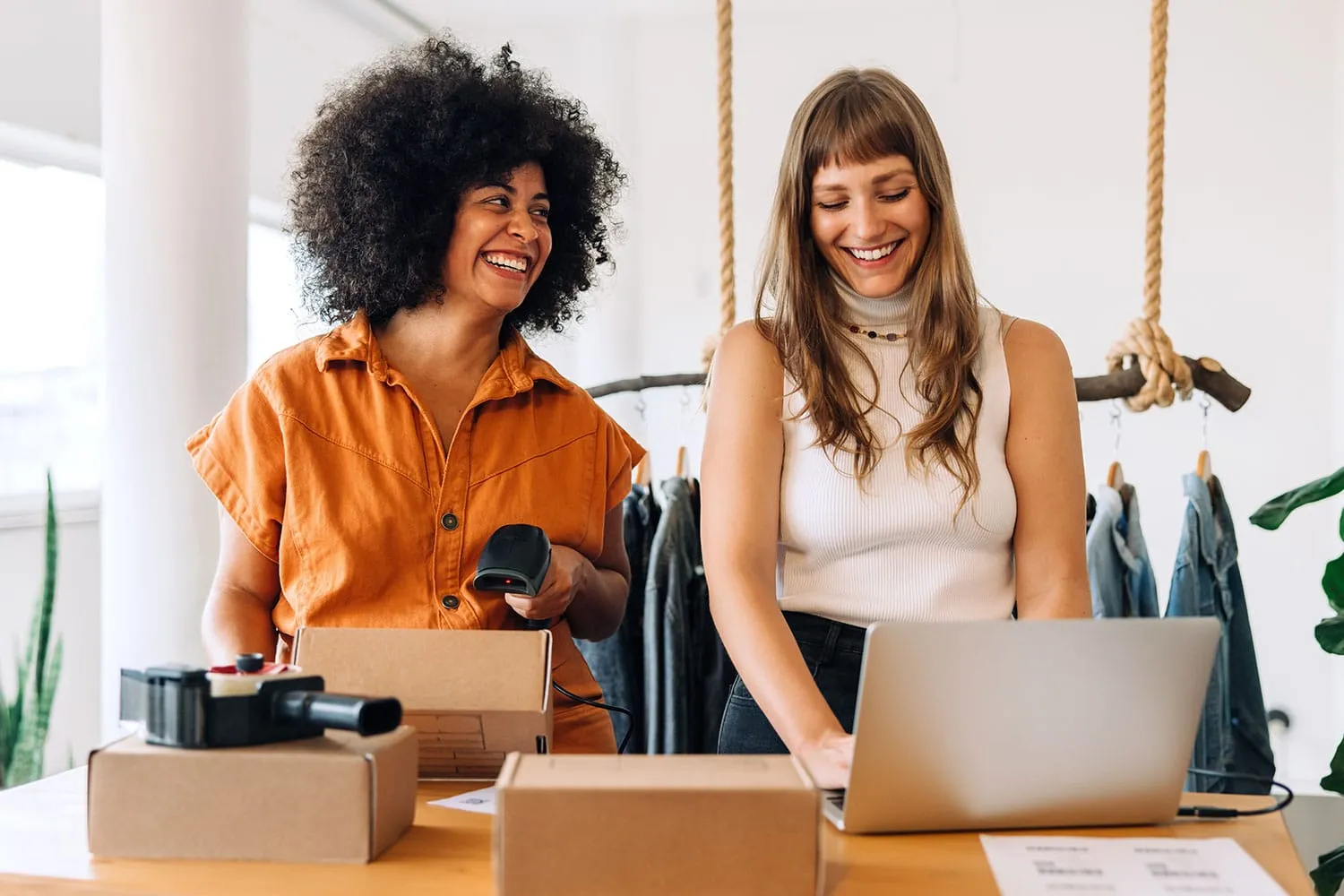Two business owners scan packages and work on a laptop while smiling at each other