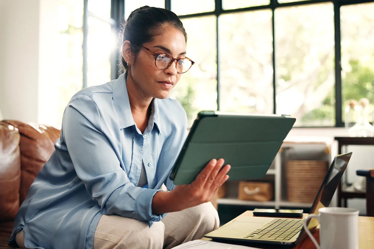 A photo of a person sitting at a kitchen table or home office desk, looking at paperwork or a laptop with a calm, composed expression