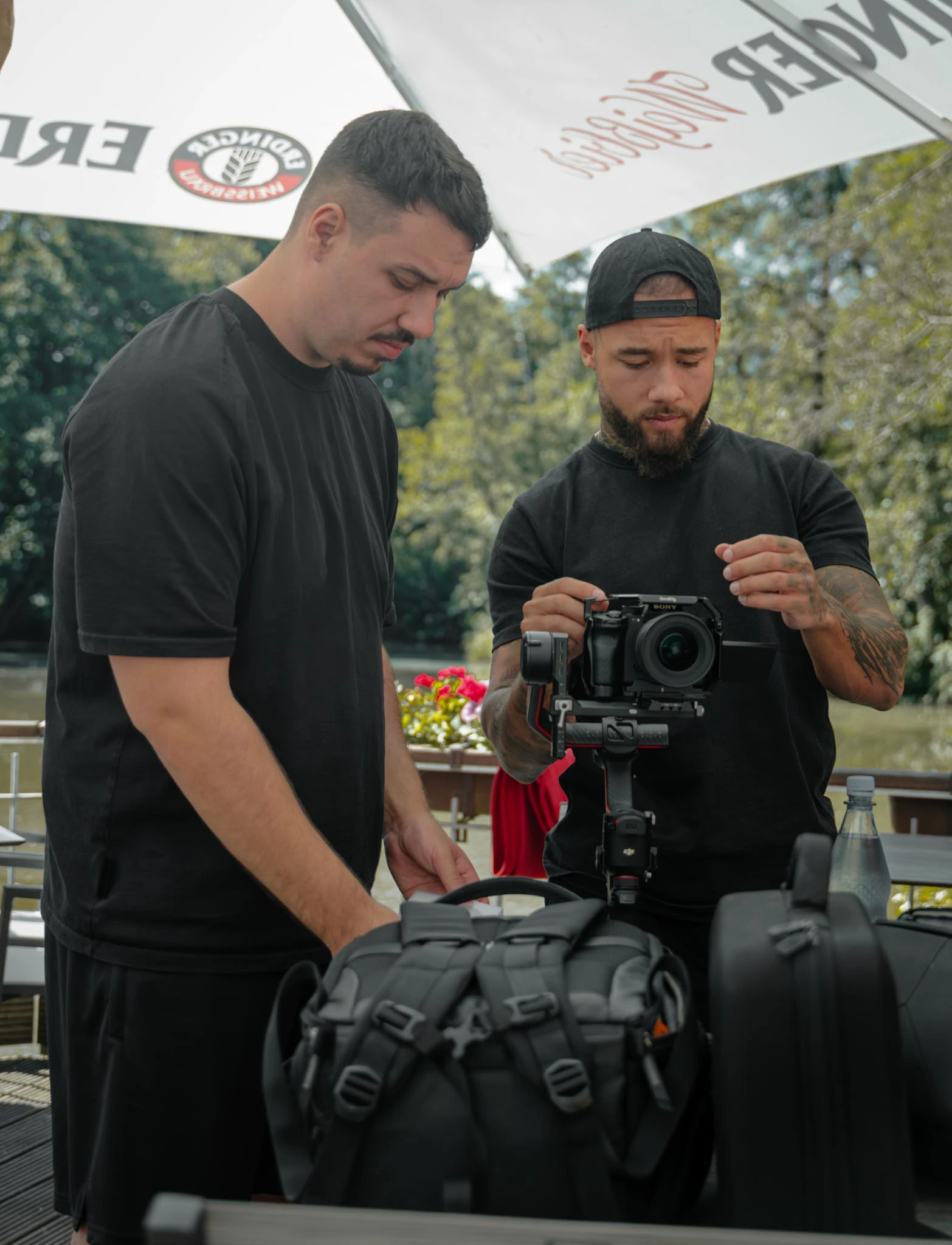 Ein Kameramann filmt mit einer professionellen Kamera, während zwei Personen im Hintergrund stehen.