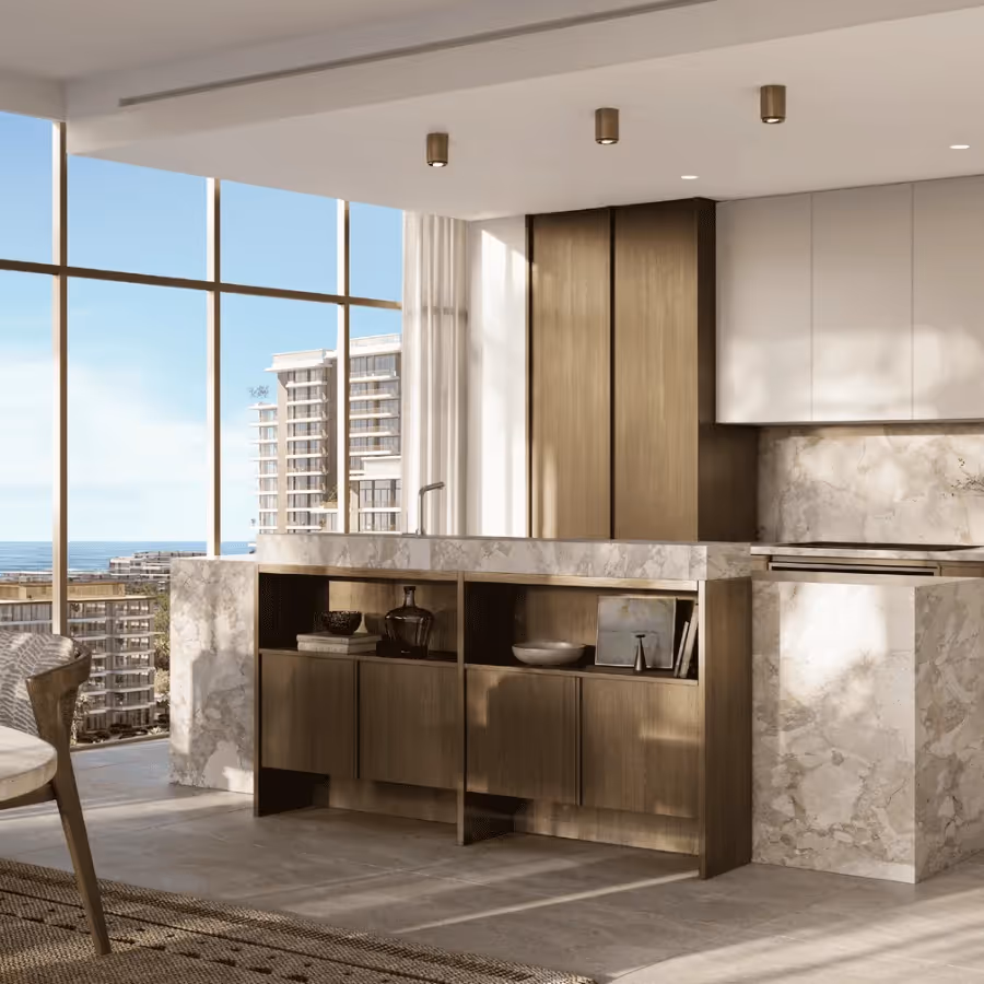 Modern kitchen with marble countertops, wooden cabinets, and large floor-to-ceiling windows overlooking city buildings and the ocean.