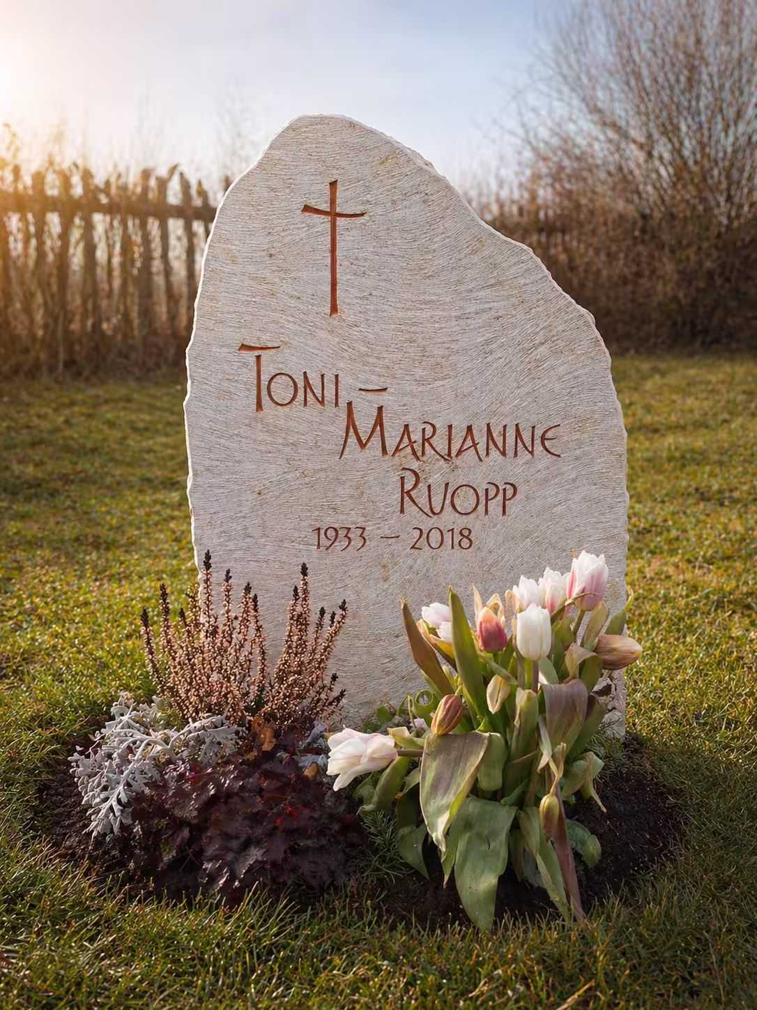 grabstein mit einer natürlichen Form und einem Kreuz auf dem bearbeiteten Stein von Hermann Naturstein auf einem Friedhof.
