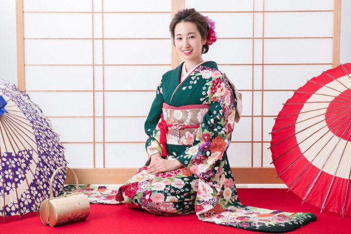Woman wearing green furisode kimono next to two umbrellas (Kimono Osaka)