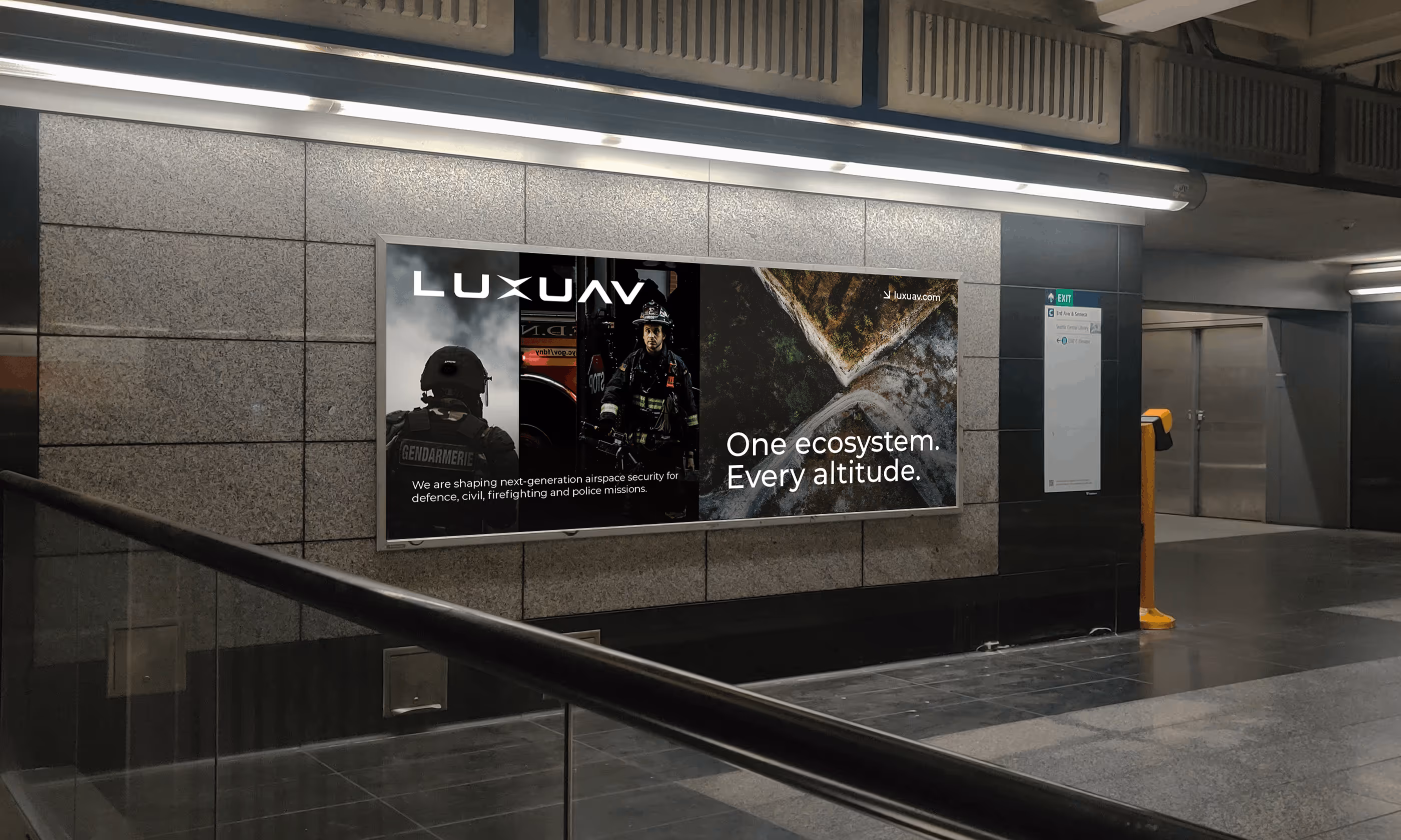 Underground station wall with an illuminated LUXUAV advertisement featuring a firefighter, a gendarmerie officer, and aerial terrain view with text about next-generation airspace security.