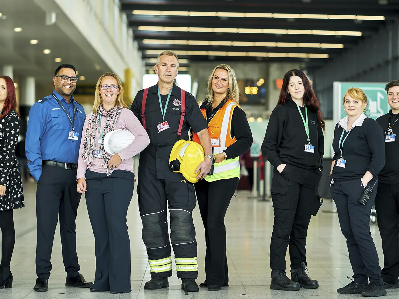 Group of seven diverse professionals in safety and security uniforms standing indoors in a brightly lit modern building.