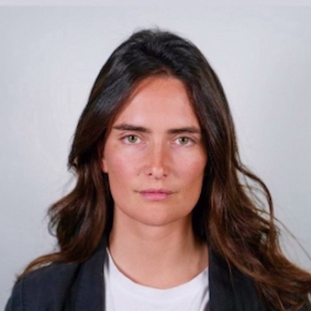 Portrait of Clara de Ros with long dark wavy hair, wearing a white t-shirt and dark blazer.