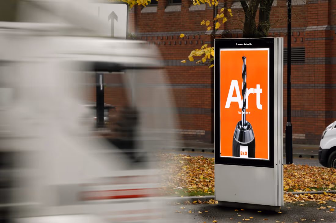 Bauer Media Outdoor digital advertising screen on a roadside displays a B&Q ad as traffic passes by.