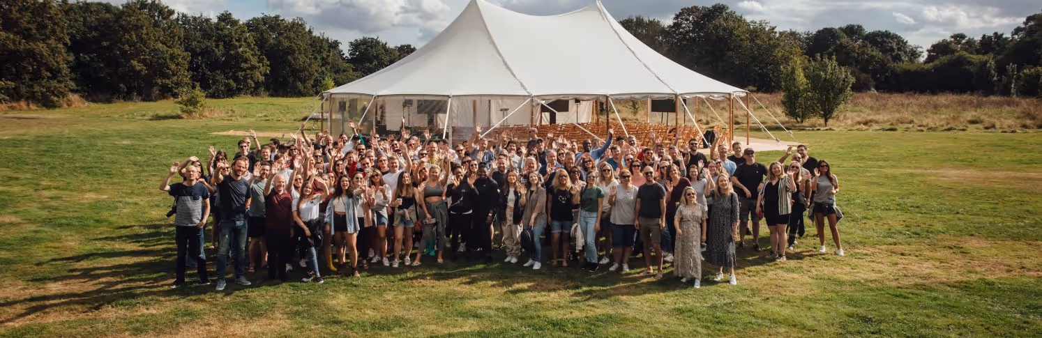 Bauer Media Outdoor employees gathered in front of a large tent and waving at the camera