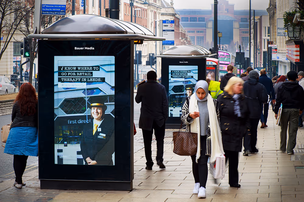 Two digital bus stop screens in Leeds with a busy high street