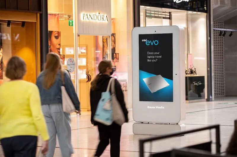Evo advert on digital screen in shopping mall with people walking past