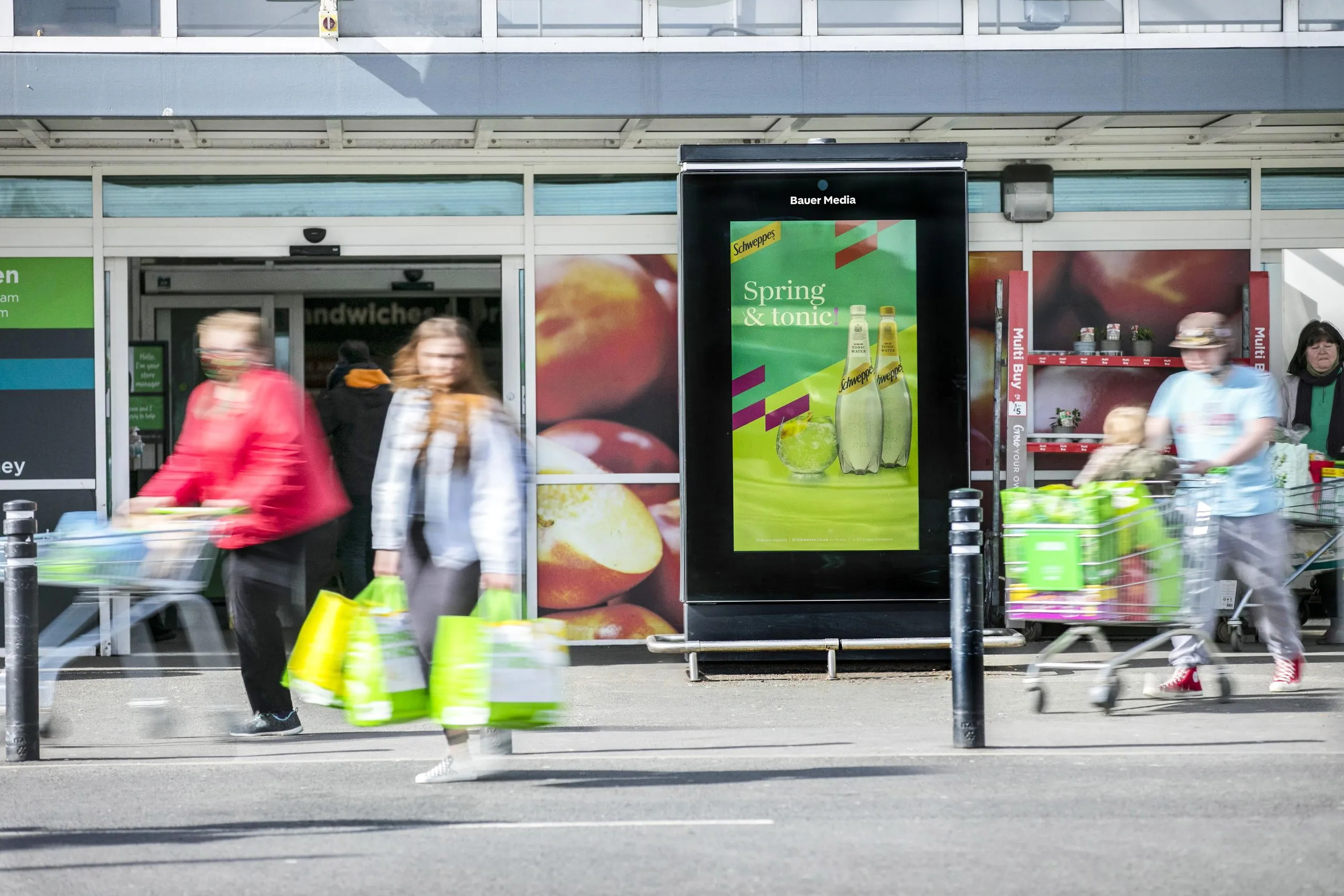 Shoppers walking in front of an Asda during an Schweppes advertisement on Asda Live