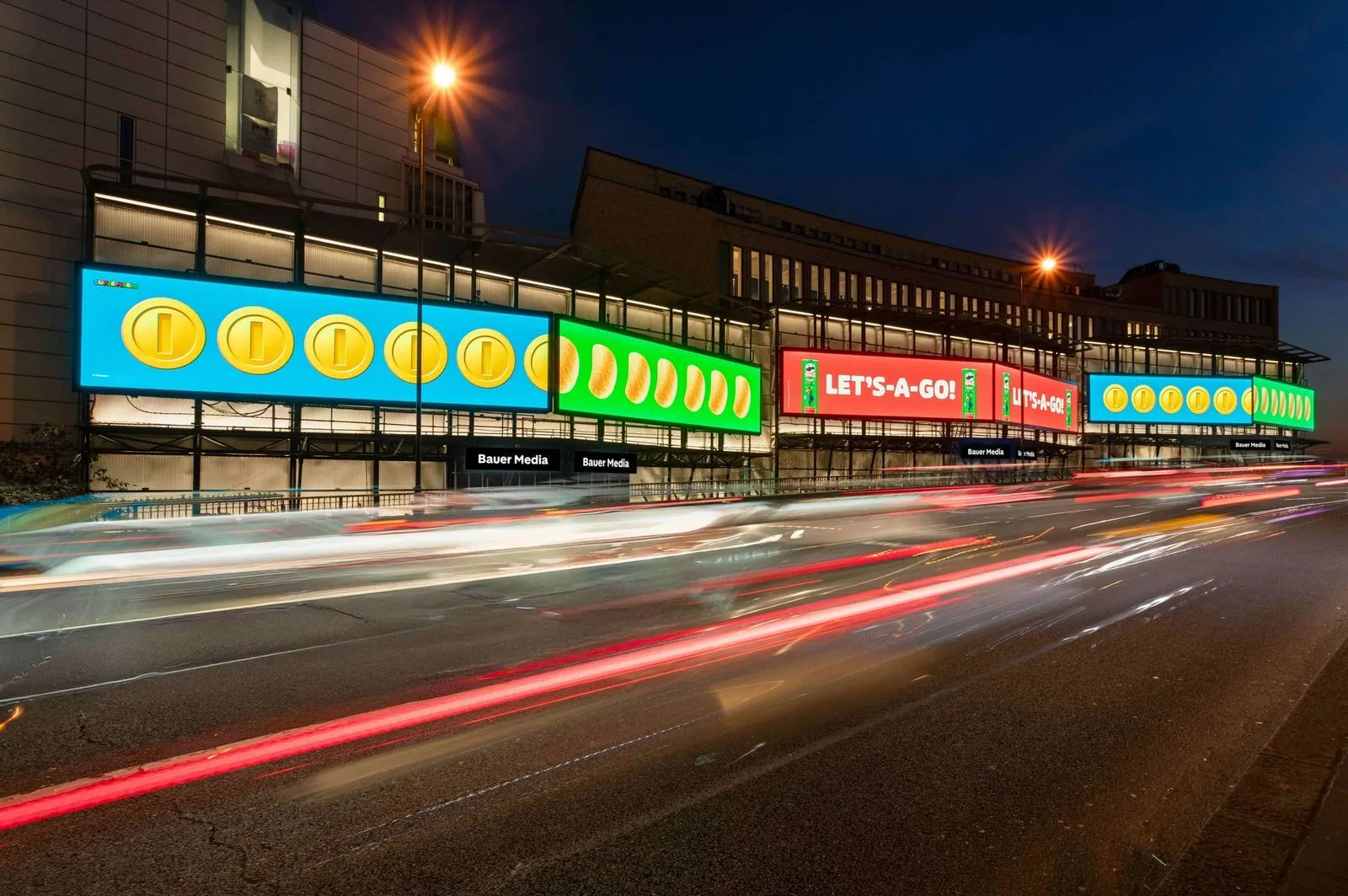 Bauer Media Outdoor digital billboard on cromwell Road displays a vibrant Nintendo Super Mario campaign with coins and the phrase “LET’S-A-GO!”, as traffic blurs past below.