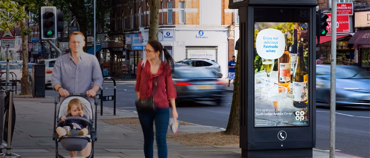 A digital screen displaying a COOP ad campaign with a family walking past