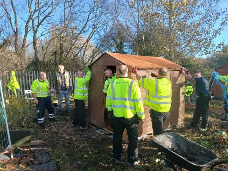 A group of men in reflective vests standing outside and working on a shed.