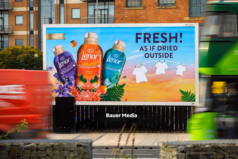 Billboard ad showing three bottles of Lenor Outdoorable fabric conditioner with flowers and clothes on a line, text reads 'Fresh! As if dried outside'.