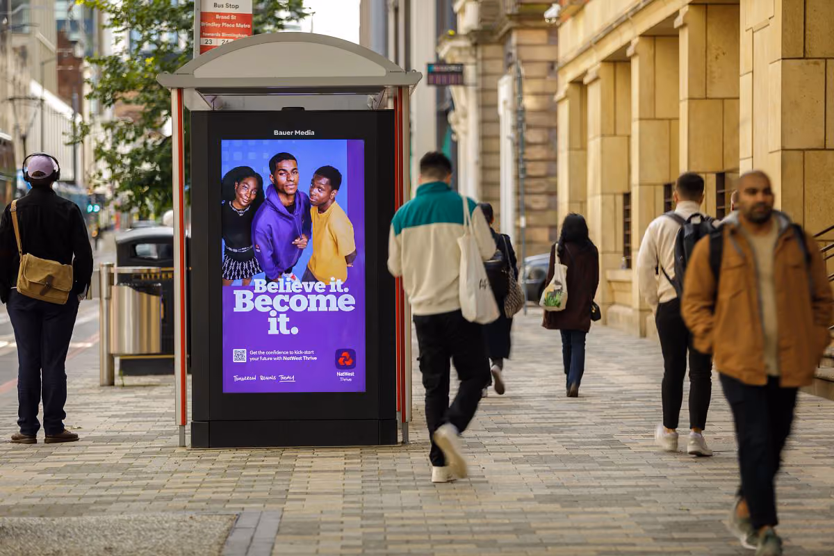A Natwest advert on a high street digital screen with people walking by