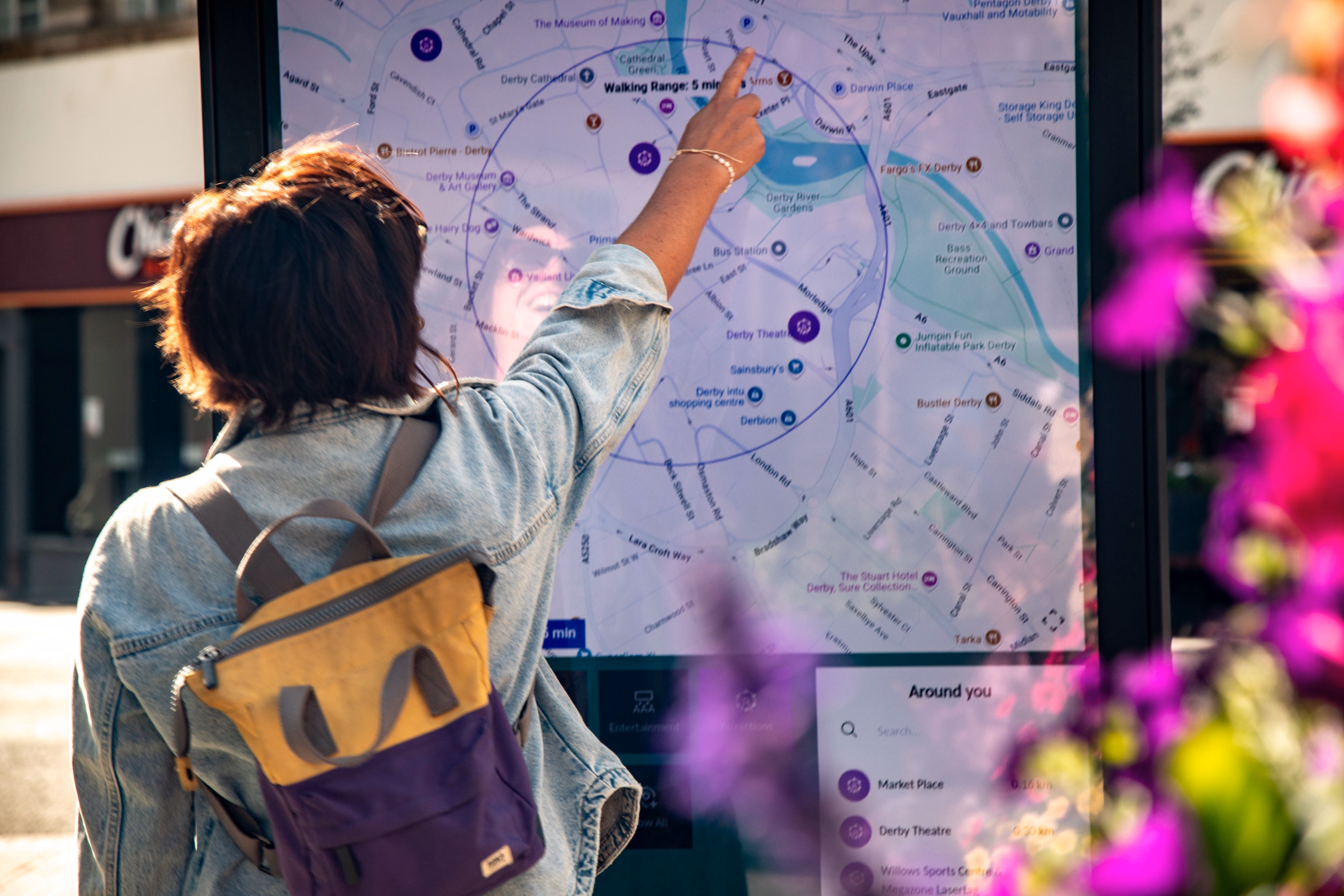 Person with a yellow and purple backpack pointing at a touchscreen map showing local landmarks and walking range.