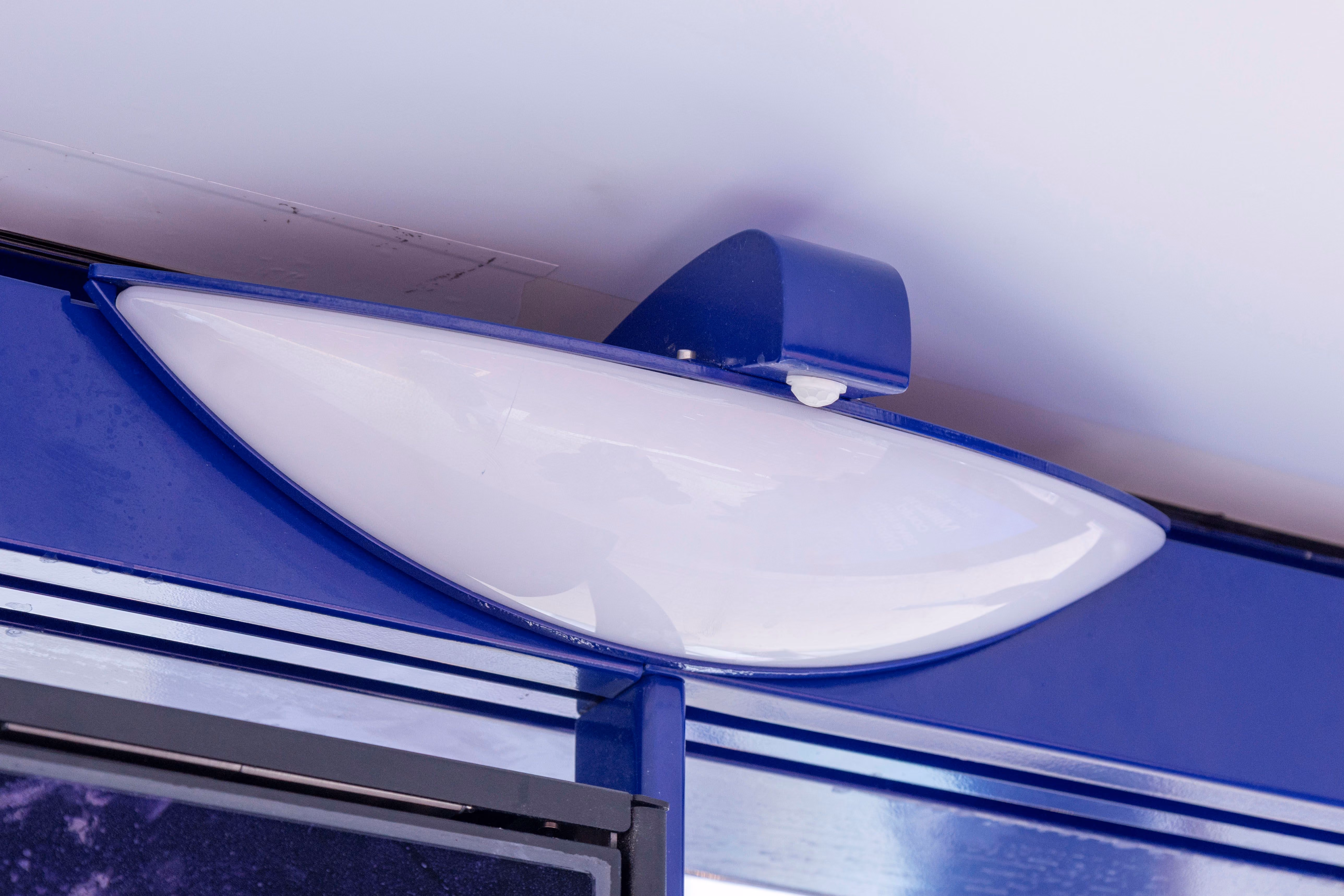 Close-up of a blue and white modern bus stop light fixture attached above a shelter.