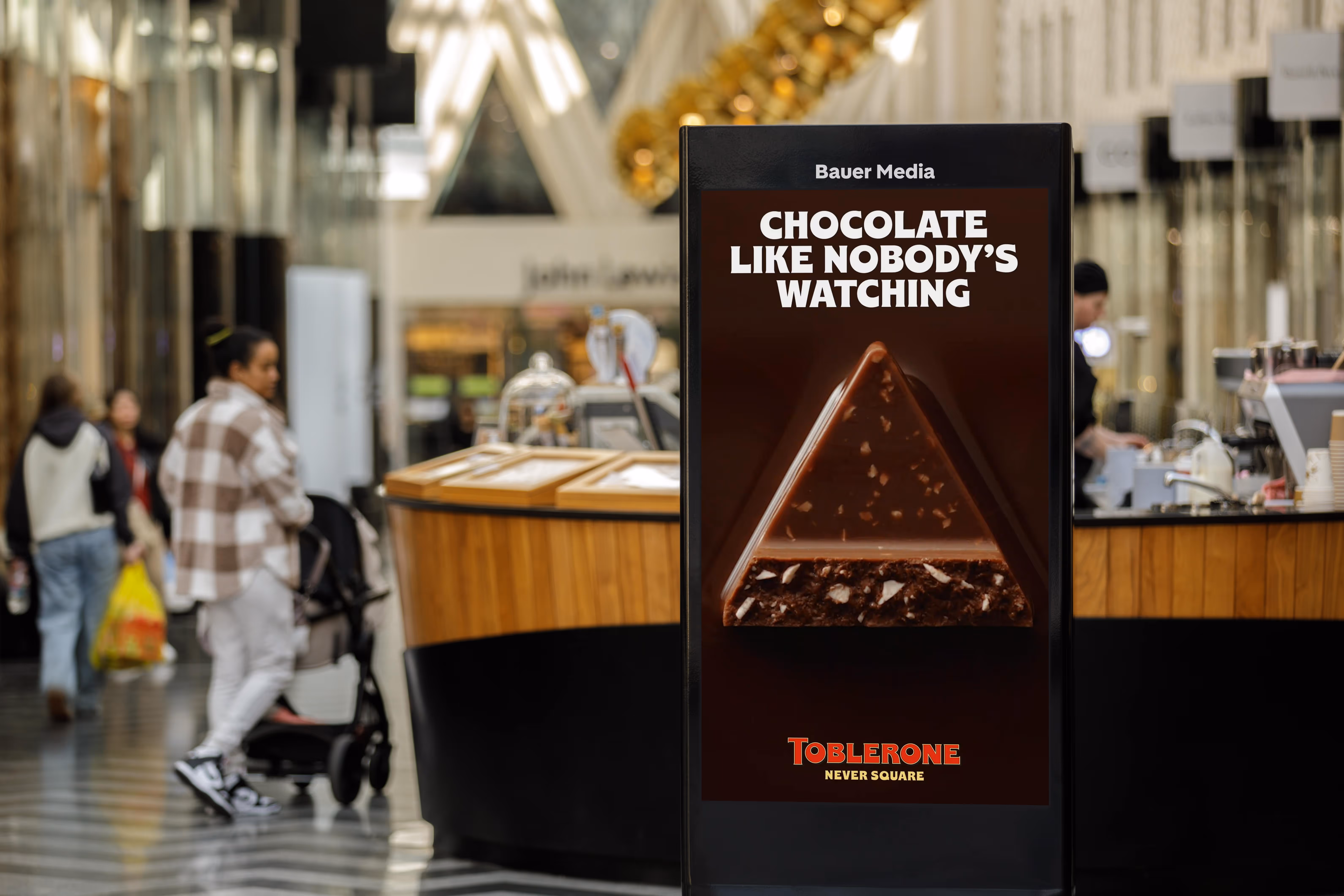 Digital display advertisement in a mall showing a Toblerone chocolate piece with the text 'Chocolate like nobody's watching' and 'Toblerone Never Square'.