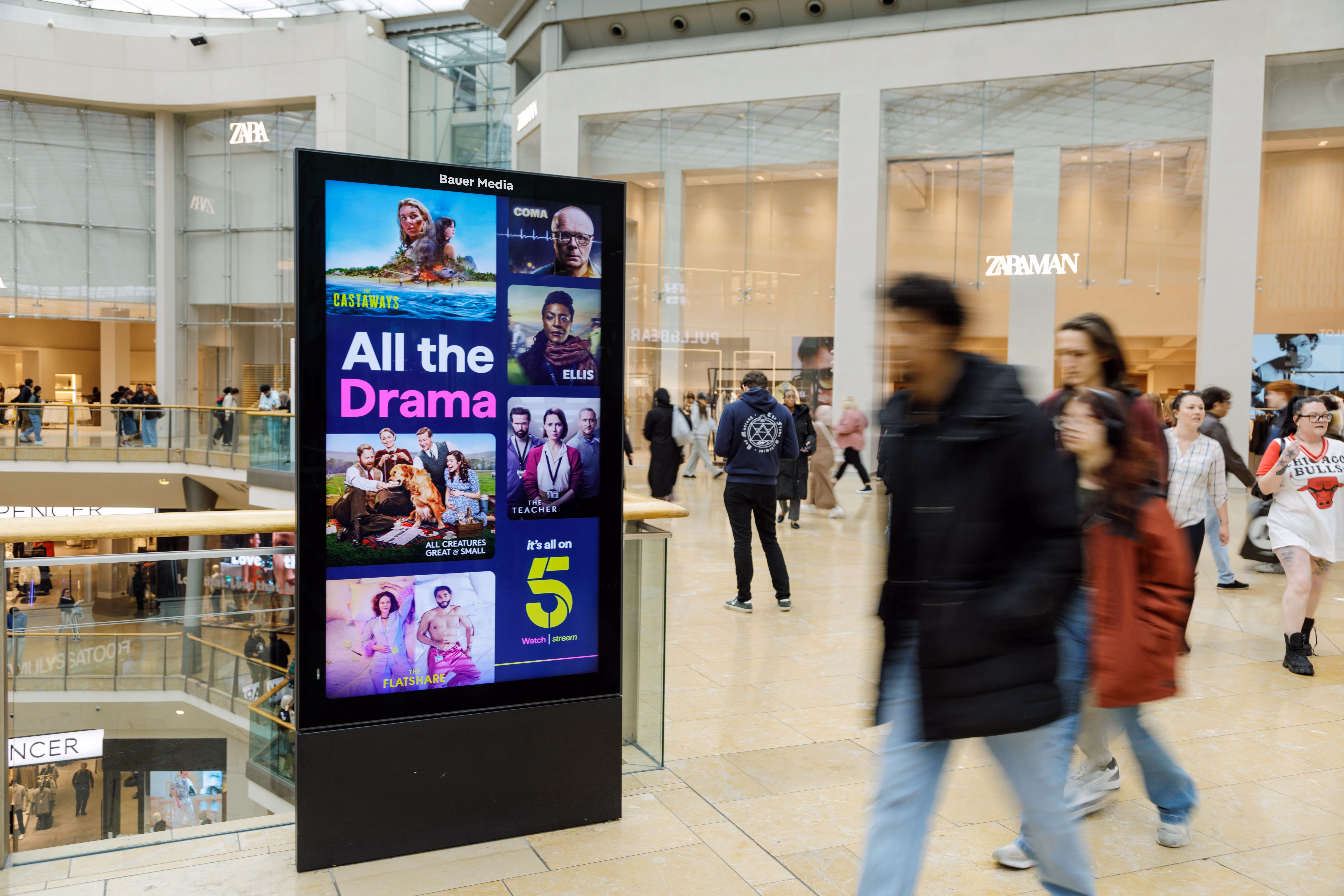 Digital advertising screen in a shopping mall displaying TV drama shows including Castaways, Coma, Ellis, All Creatures Great and Small, The Teacher, and The Flatshare.