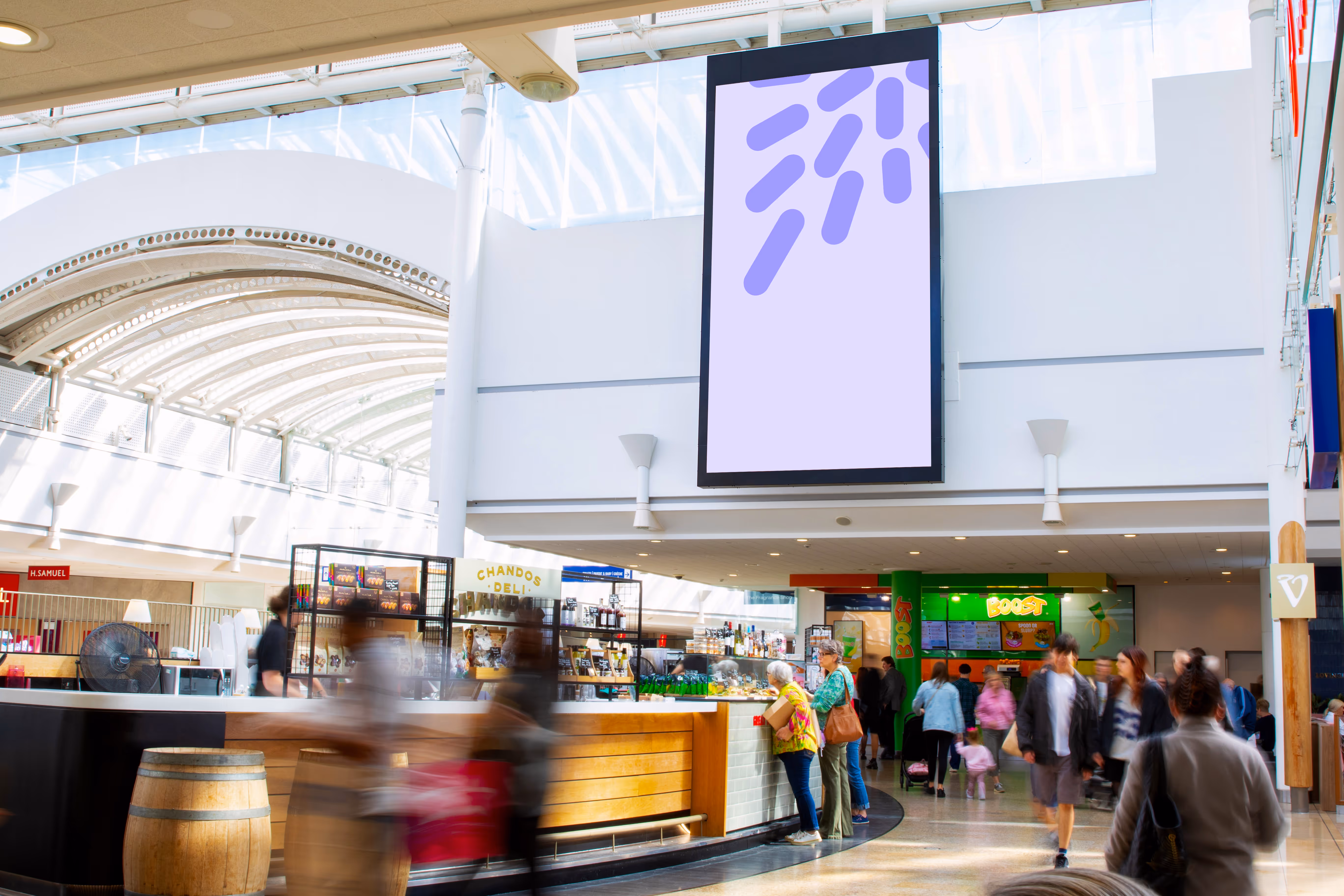 Bright shopping mall atrium with a deli counter, shoppers walking, and a large blank digital advertising screen overhead.
