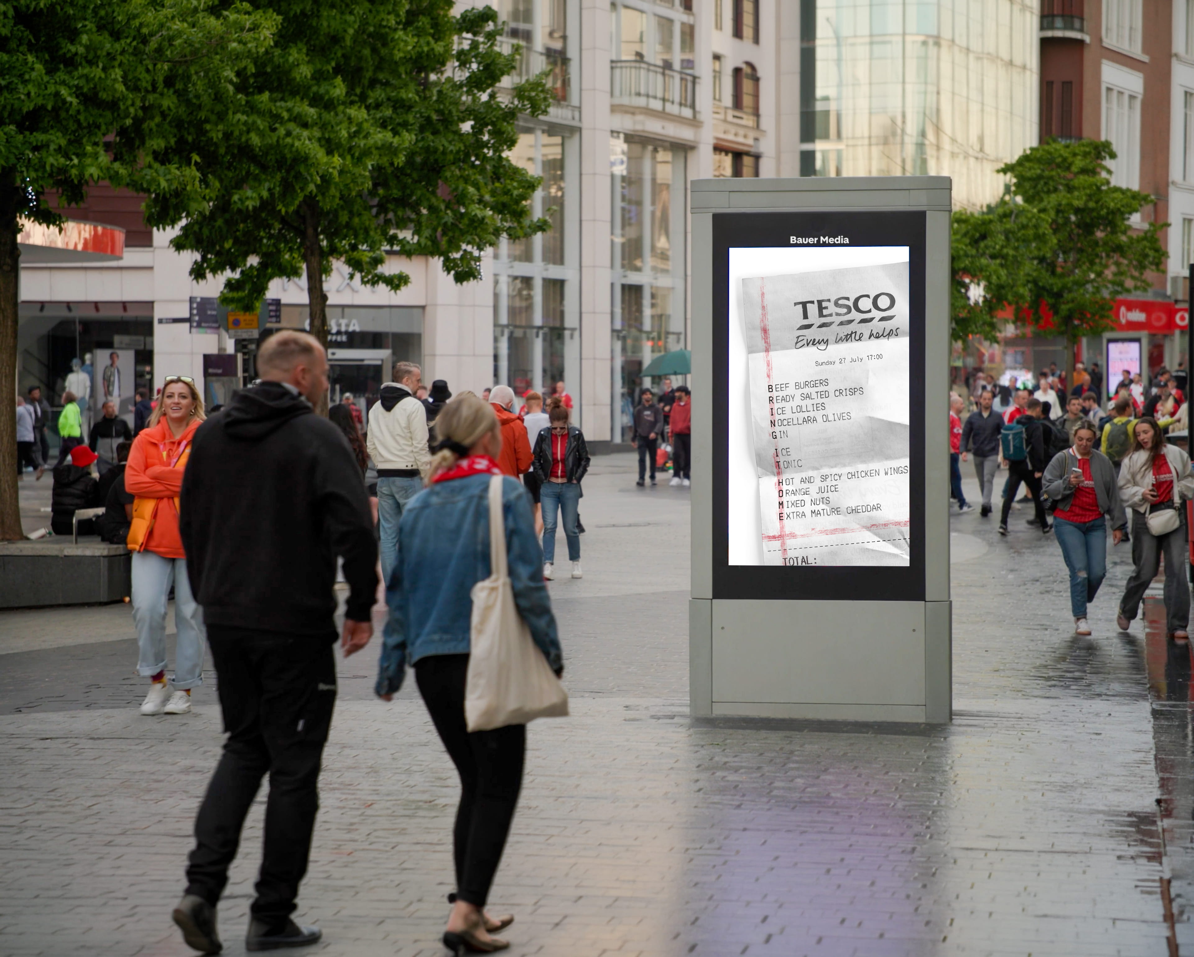 Outdoor digital billboard in a busy city street showing a Tesco receipt with grocery items listed.