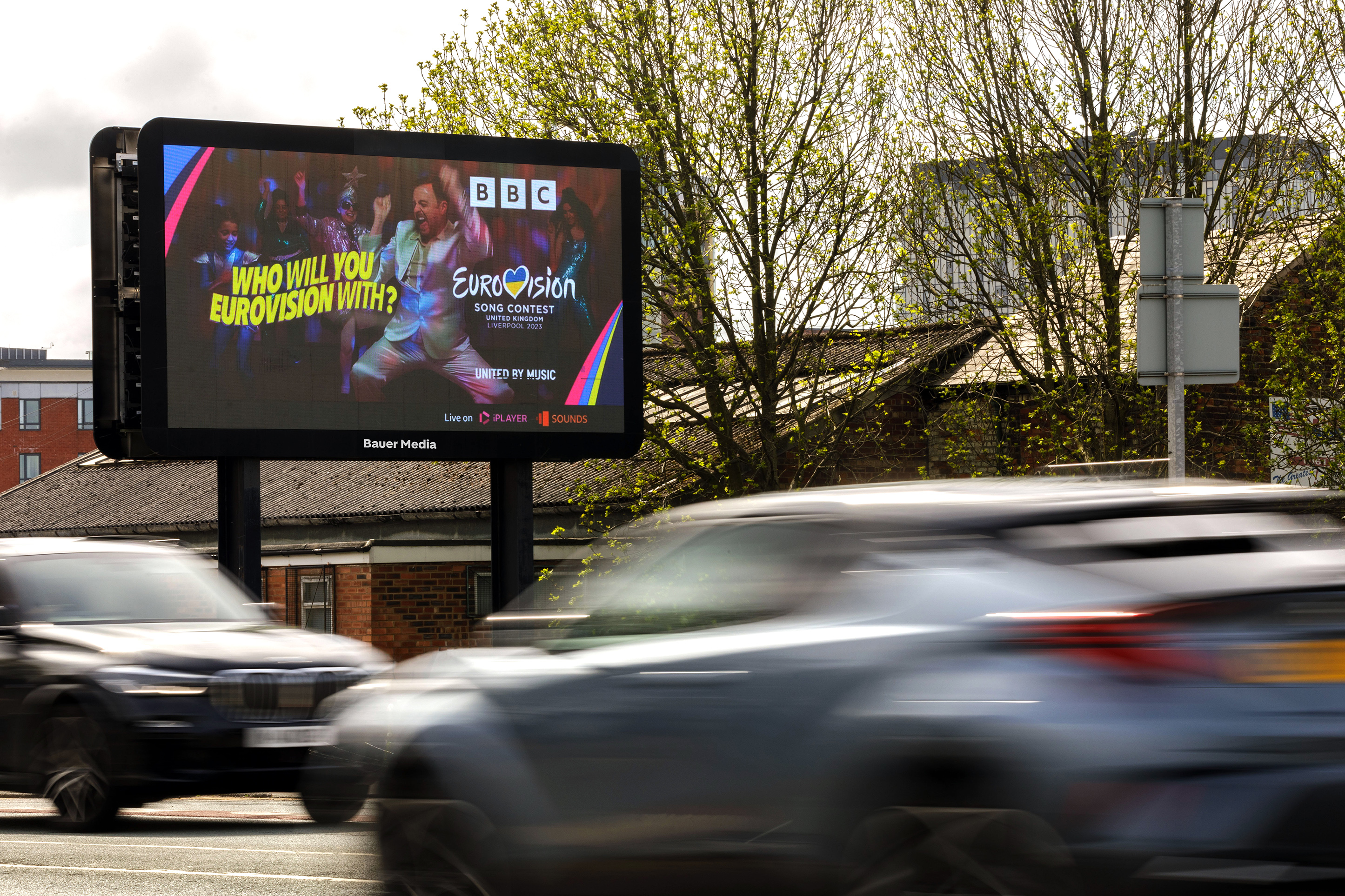 Digital billboard by a roadside displaying a BBC Eurovision Song Contest promotion with dancers and text 'Who will you Eurovision with?'