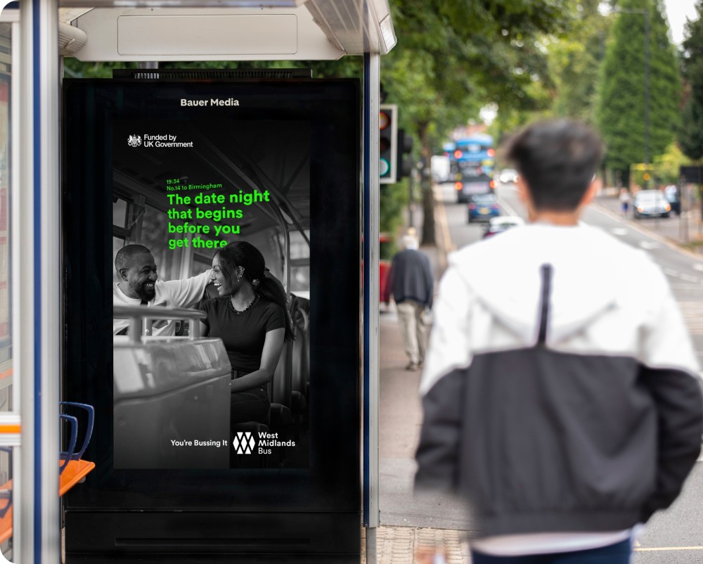 Bus shelter advertisement showing a smiling couple inside a bus with text promoting West Midlands Bus service.
