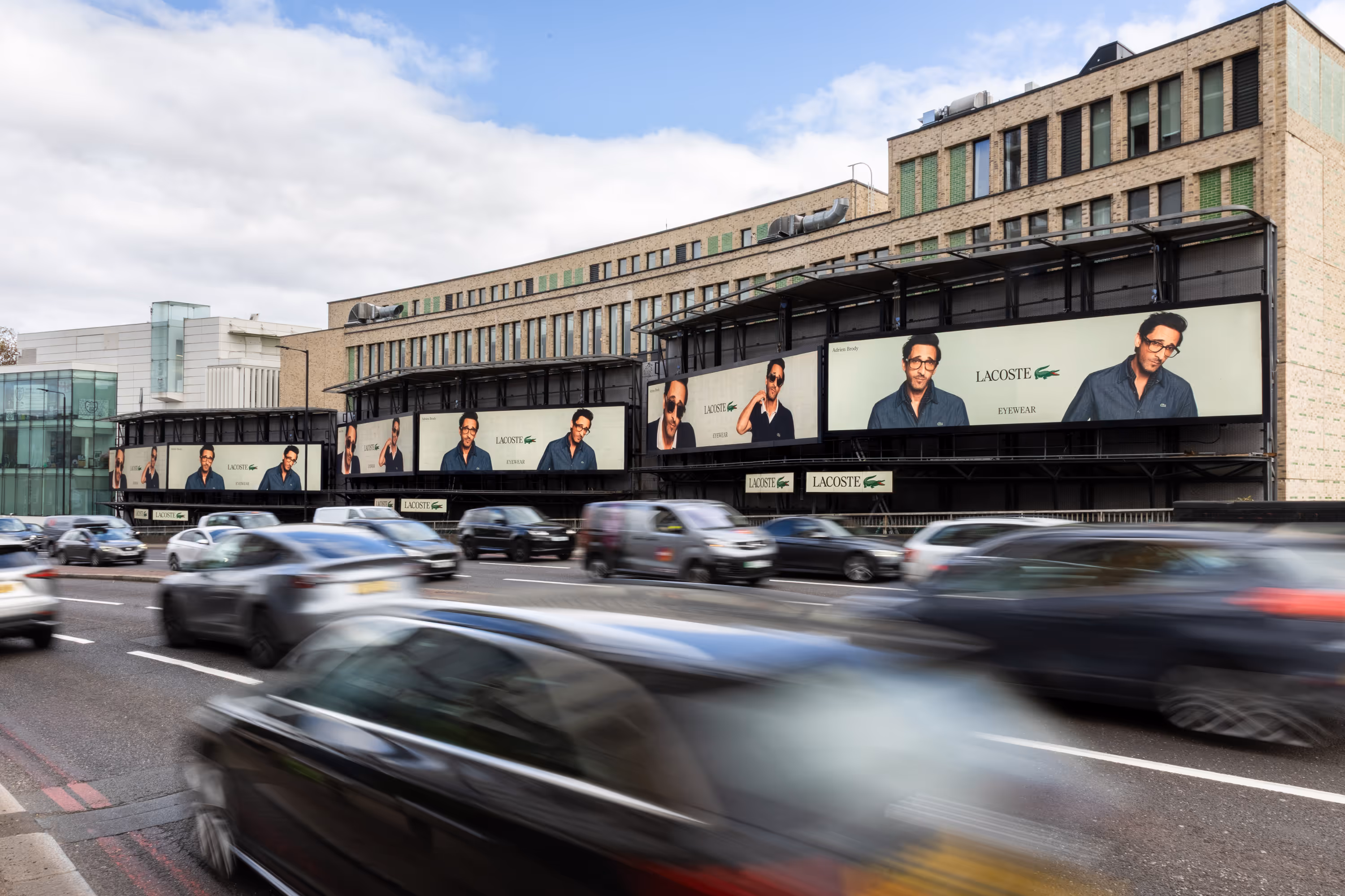 Multiple Lacoste Eyewear billboards with a man wearing glasses above a busy multi-lane road.