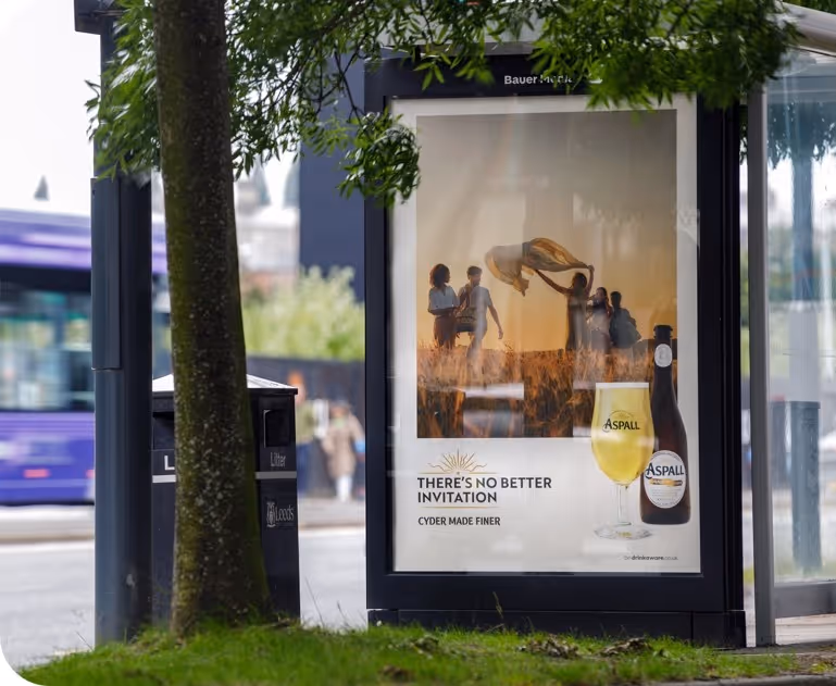 Bus stop advertisement for Aspall cyder showing a group of people enjoying a sunny outdoor scene with a bottle and glass of Aspall cyder alongside the slogan 'There's no better invitation, cyder made finer.'