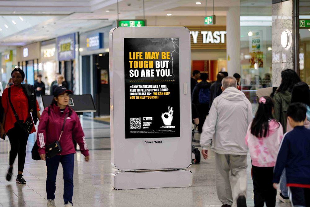 Digital poster in a mall displaying a motivational message about toughness and peer support for men over 18.
