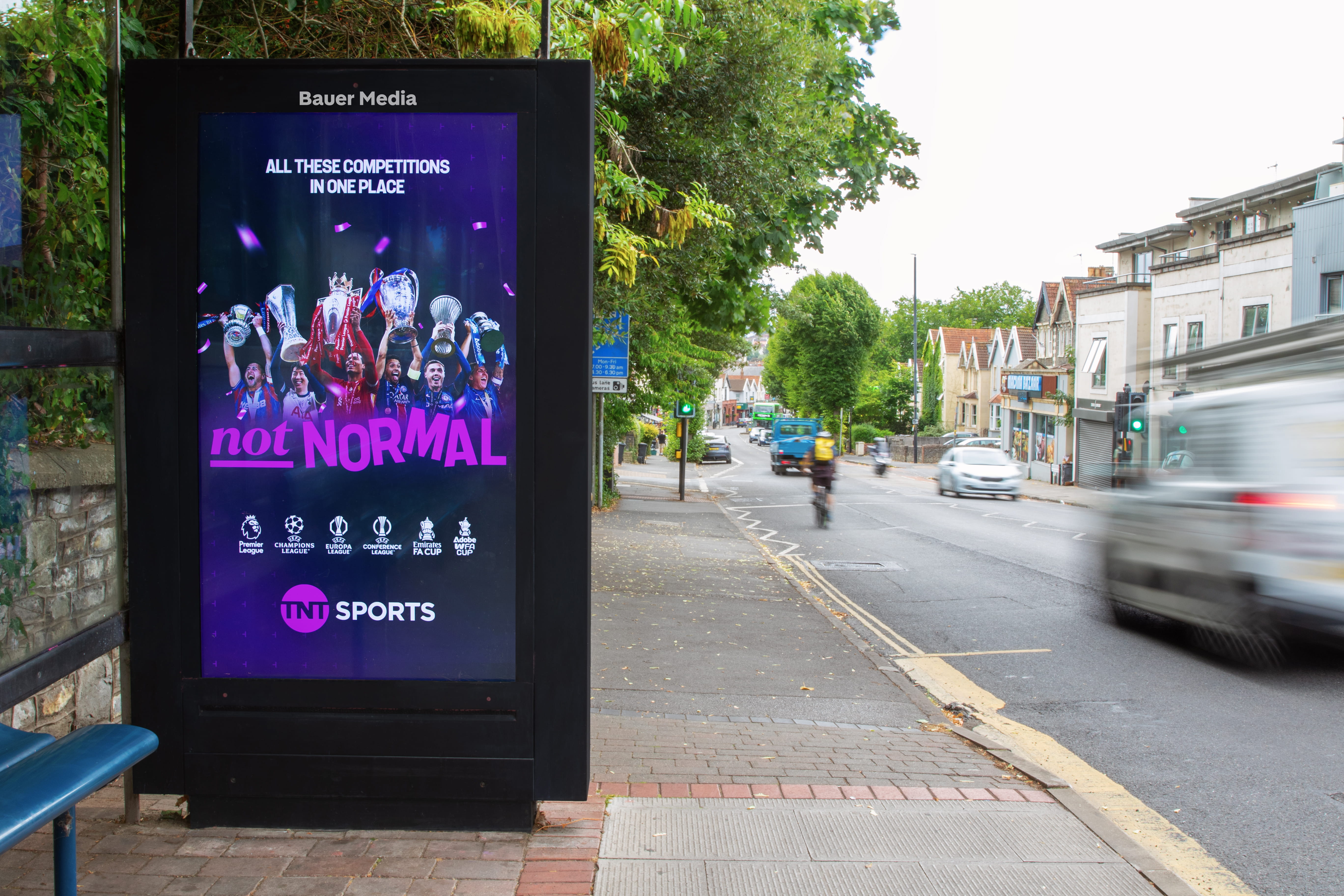 Bus stop digital ad displaying football players holding trophies with text 'All these competitions in one place, not normal' and TNT Sports logo.