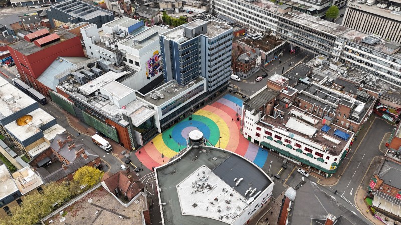 Aerial view of an urban area showing buildings and a large rainbow-colored circular pattern painted on the pavement.