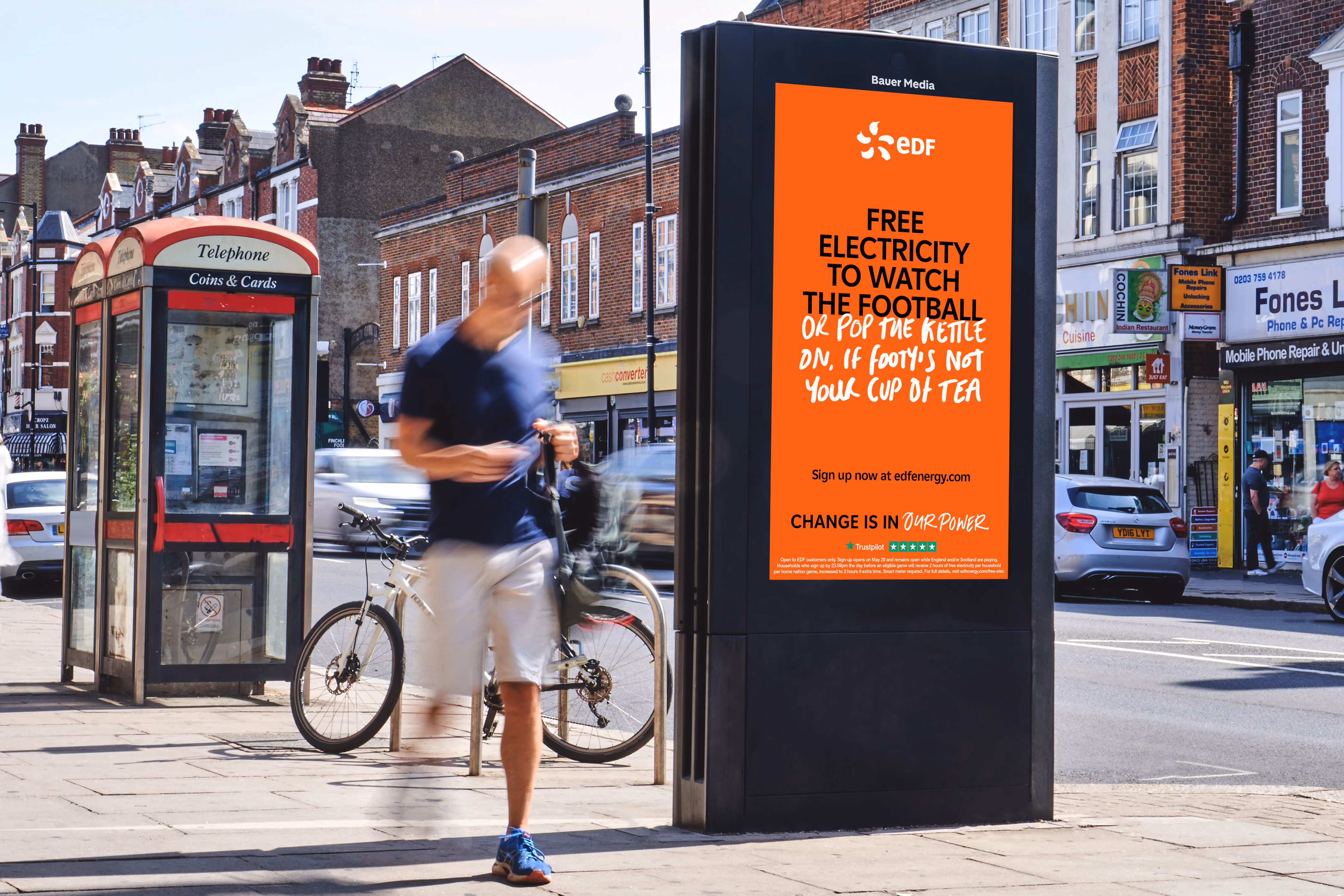 Street scene with a man walking by a phone booth and an EDF ad offering free electricity to watch football.