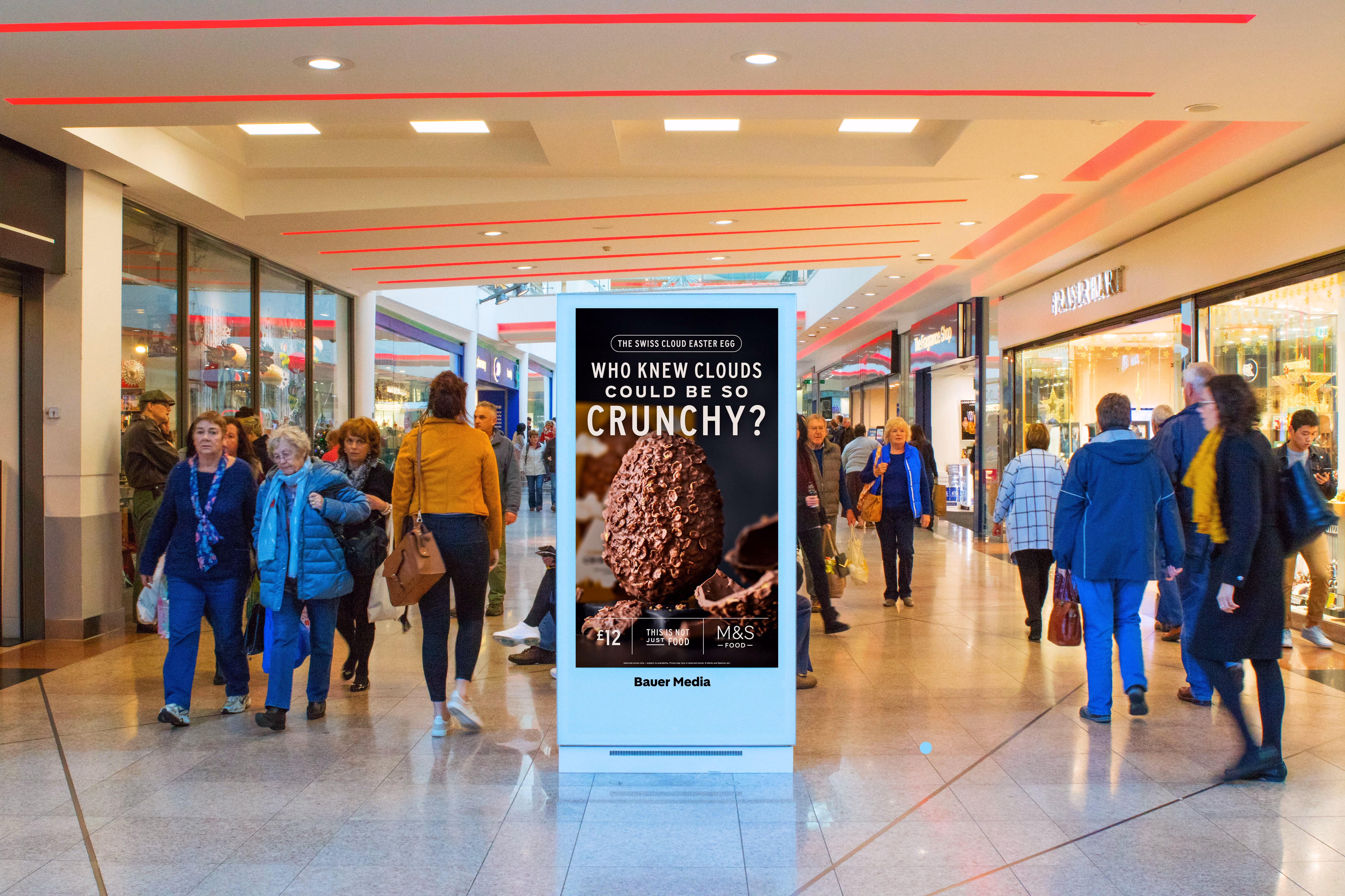 Shopping mall with people walking past a digital ad for a crunchy Swiss cloud Easter egg at M&S