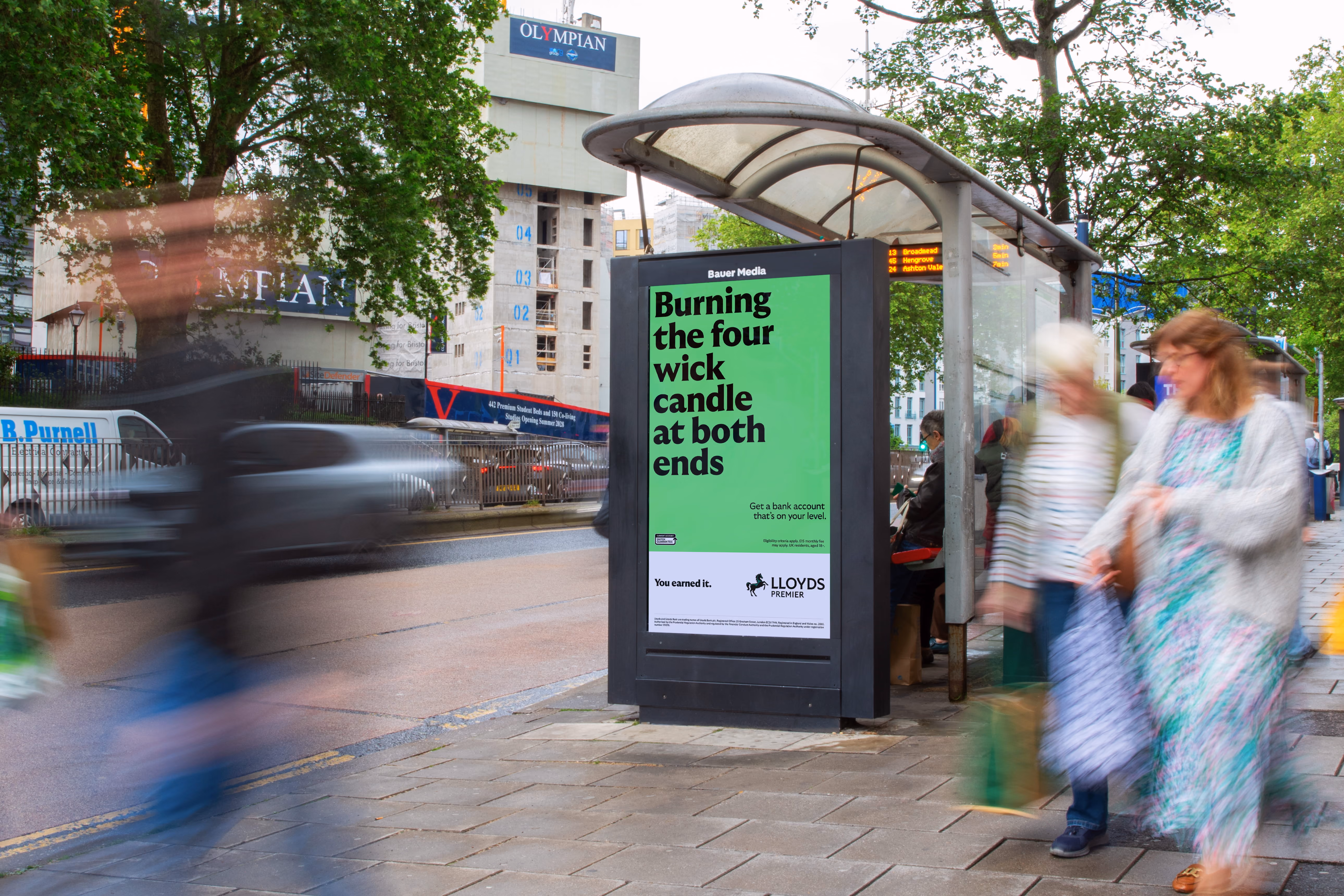 Bus shelter with an ad reading Burning the four wick candle at both ends by Lloyds Premier bank.