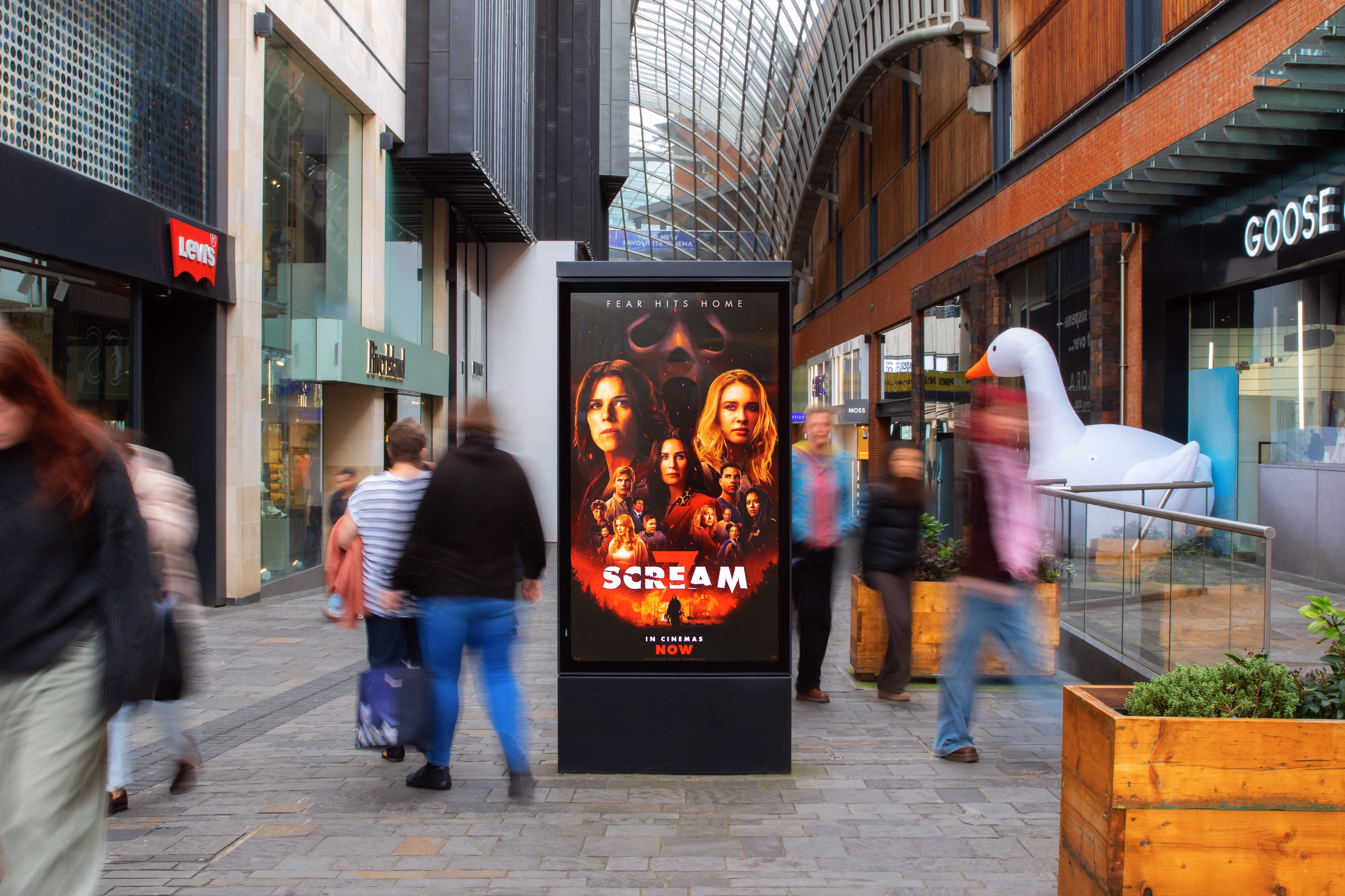 Movie poster for Scream displayed on a city sidewalk with blurred pedestrians walking by.