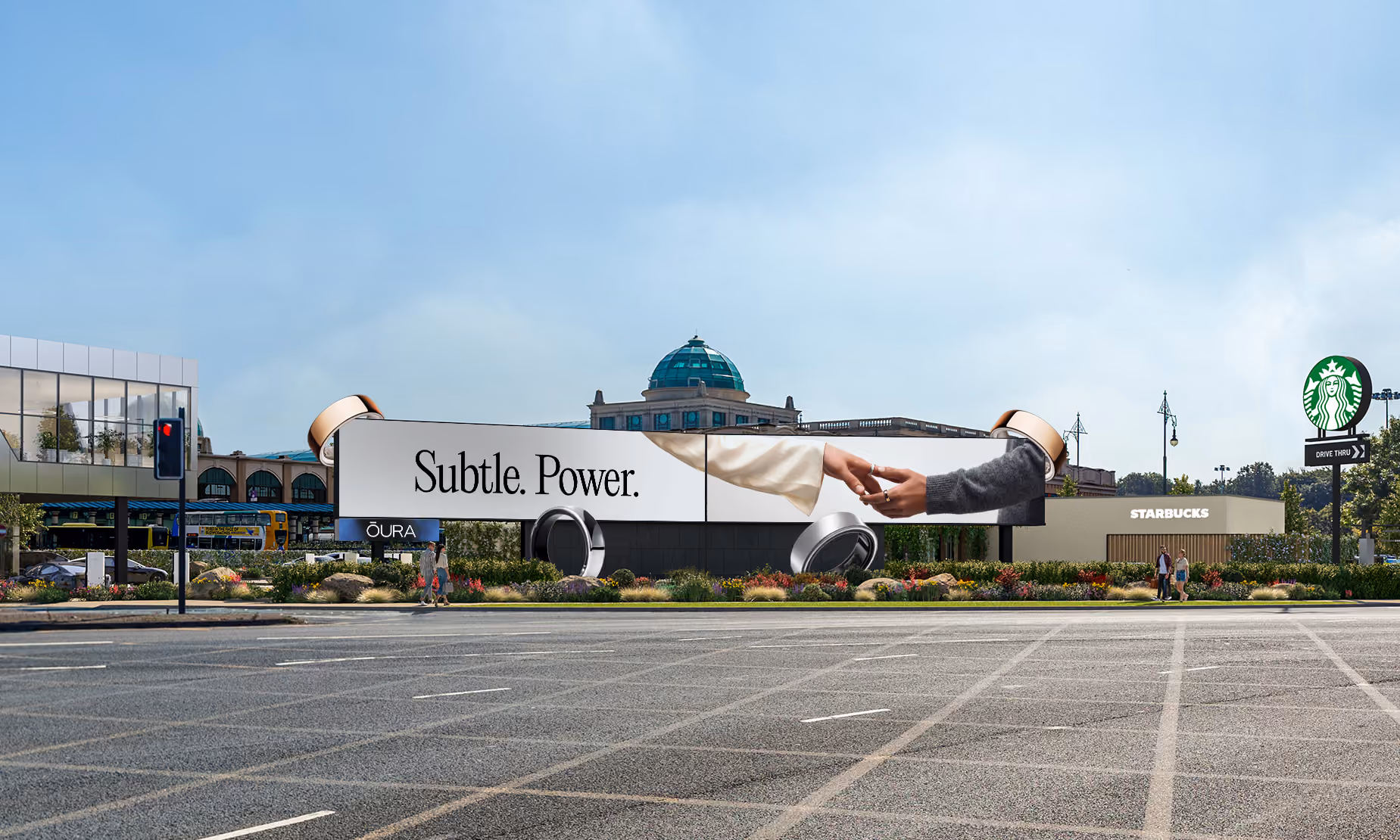 Outdoor billboard advertisement for OURA featuring a large image of two hands reaching to touch each other with the text 'Subtle. Power.' The billboard is set in an urban area with a Starbucks coffee shop and a green dome building in the background.