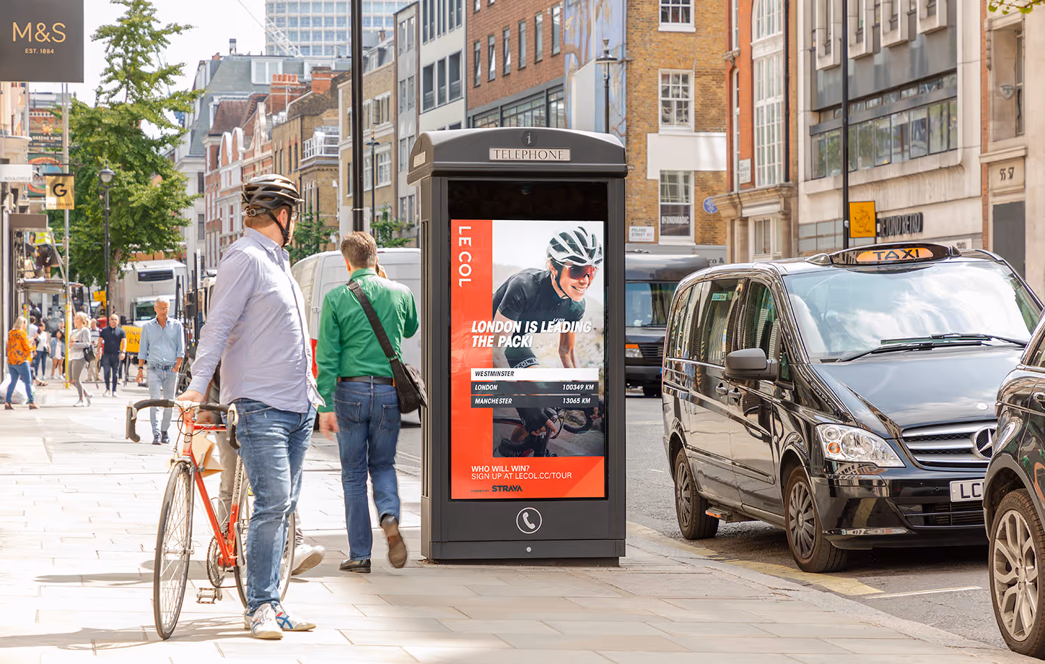 A cyclist on the pavement looking at a Le Col cycle campaign on an Adshel Live panel