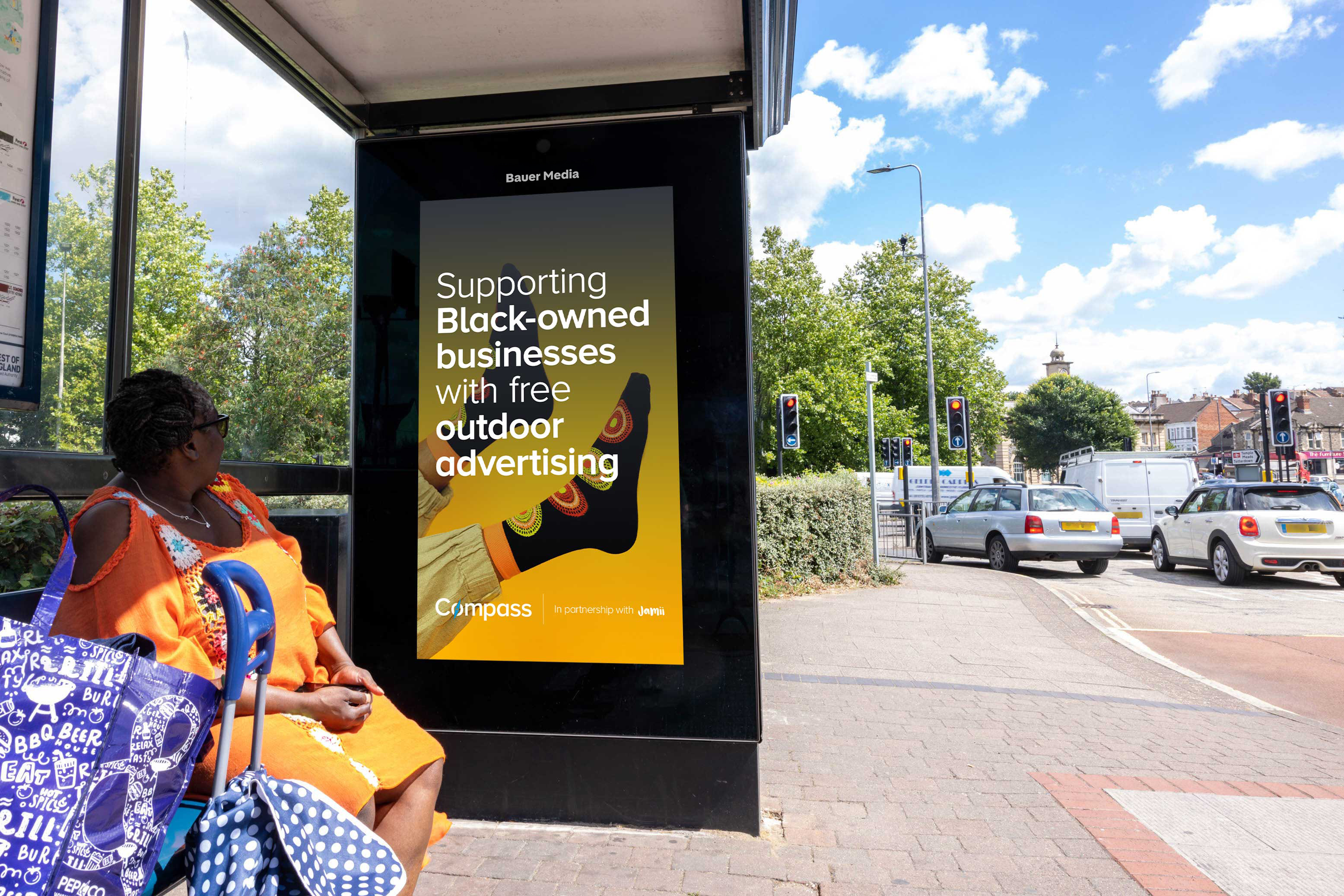 A woman sitting at a bus shelter by a busy road, during the day, that features Compass advertising