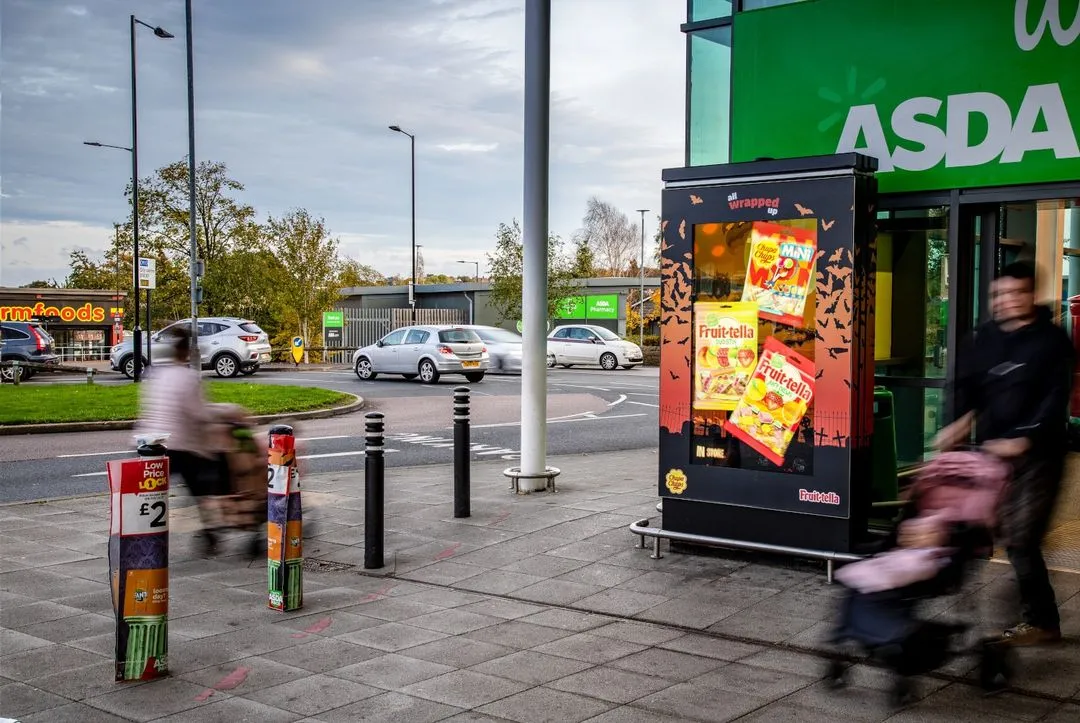 Perfetti Halloween advert on a digital screen, outside an Asda, as shoppers walk in and out during the day